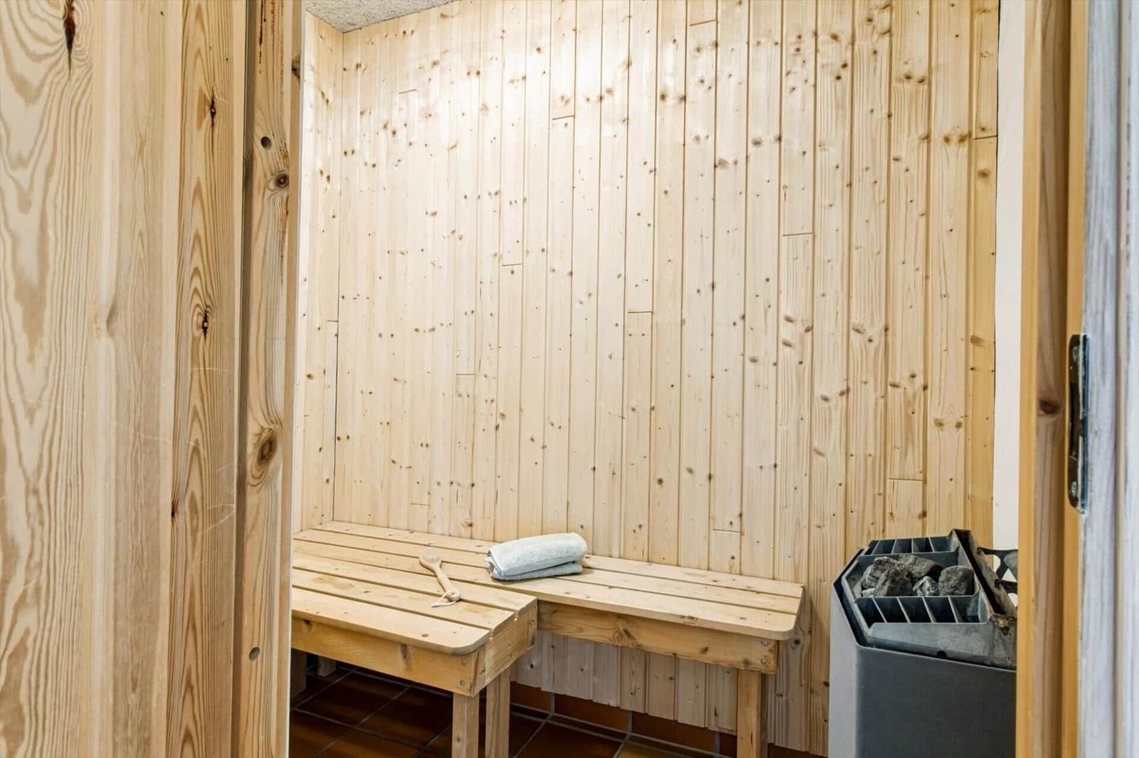 Sauna mit Holzwand, Bank und Steinheizung. Handtuch und Bürste liegen bereit.