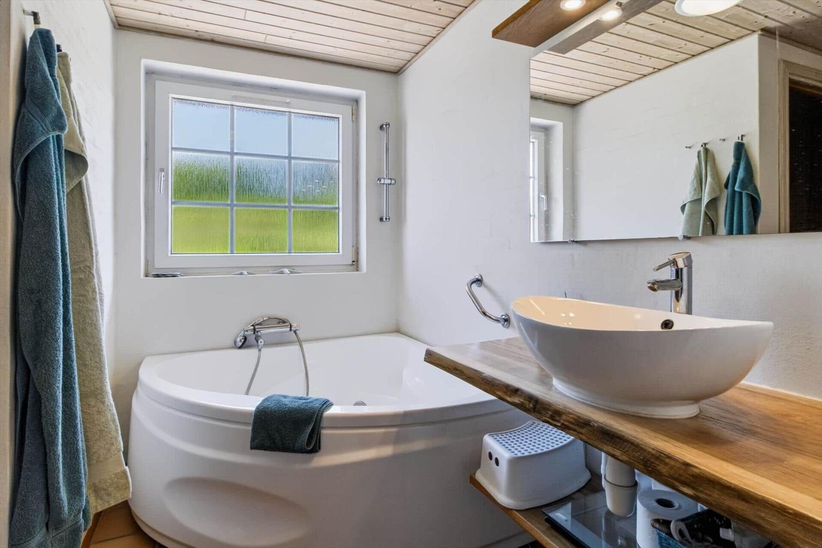 Bad mit Badewanne, Waschbecken und Fenster mit Blick auf Gras.