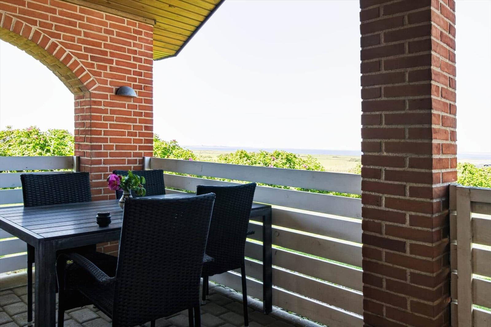 Terrasse mit Tisch und Stühlen, Blick auf Landschaft und Meer.