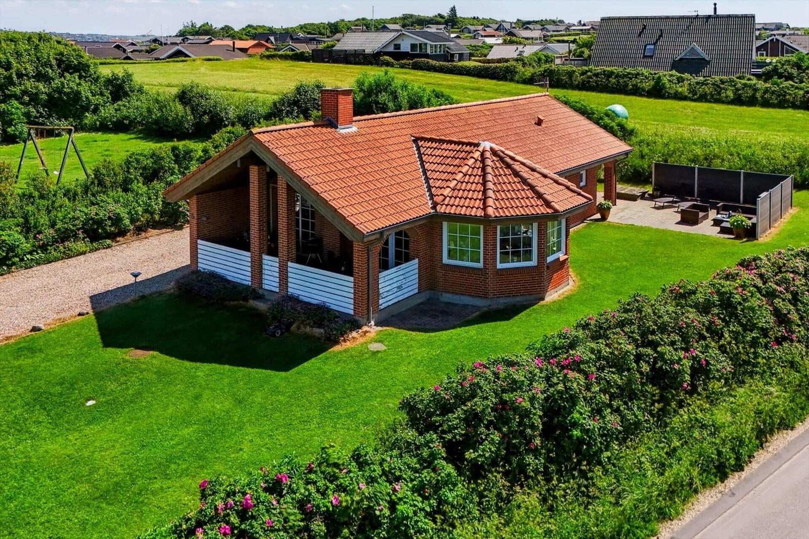 Ein rotdachiges Haus mit weißem Sichtschutz, umgeben von Grünfläche und Gartenmöbeln.