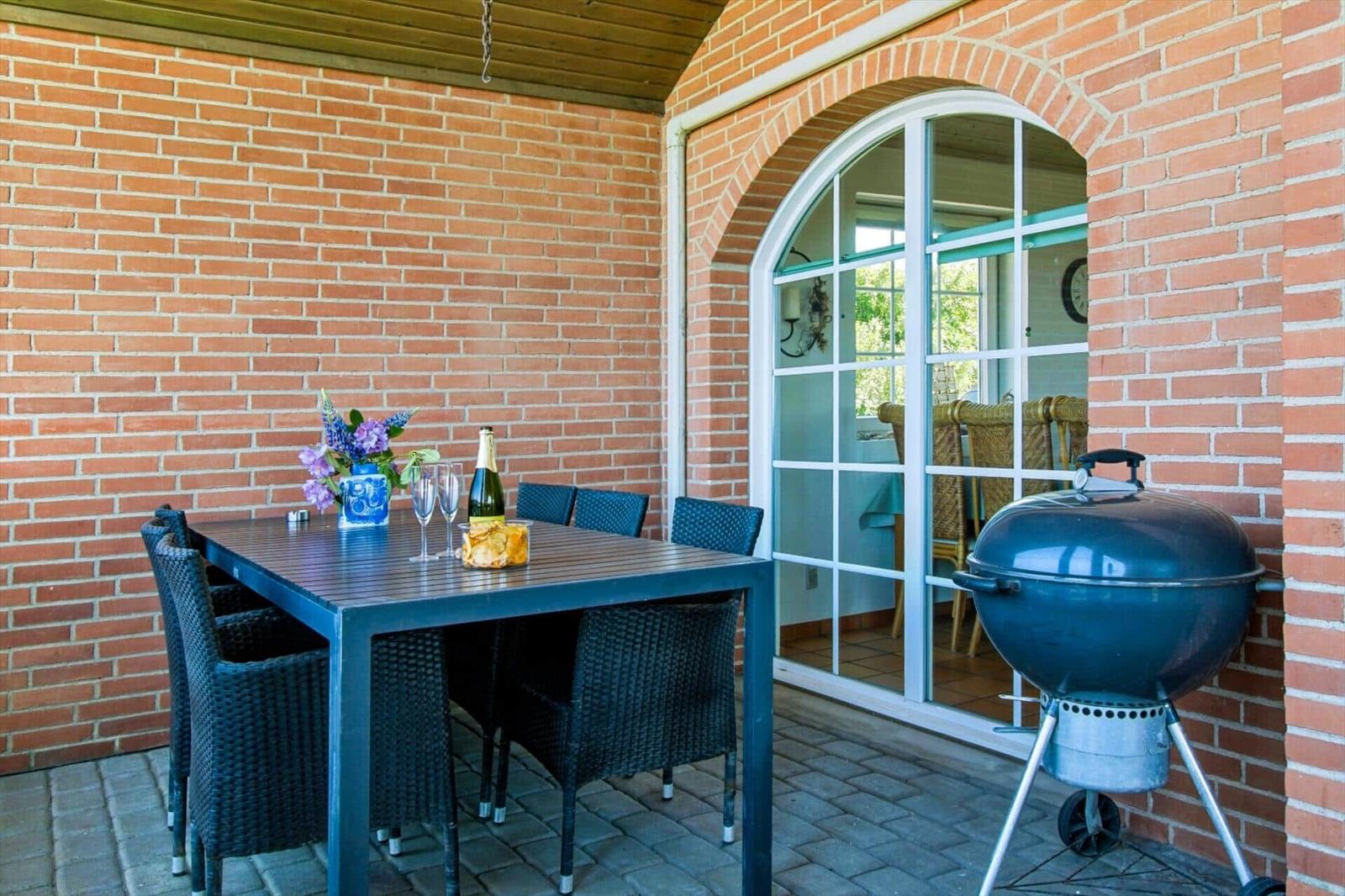Terrasse mit Tisch, Stühlen, Grill und Blick ins Haus.