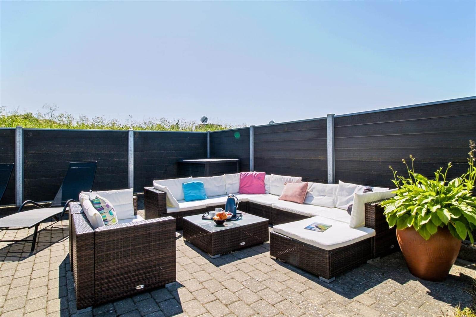 Terrasse mit Sitzgruppe, Tisch und Pflanze. Hintergrund: Holzumzäunung und Himmel.