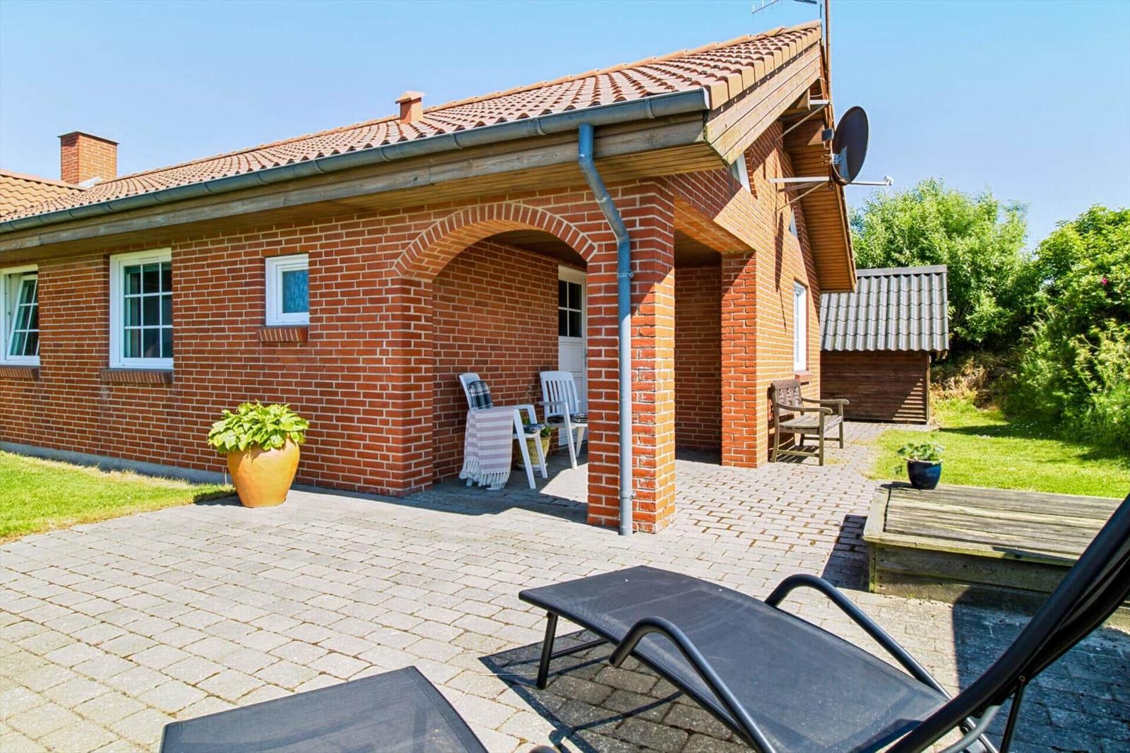 Rotes Backsteingebäude mit Terrasse und Liegestühlen im Garten.