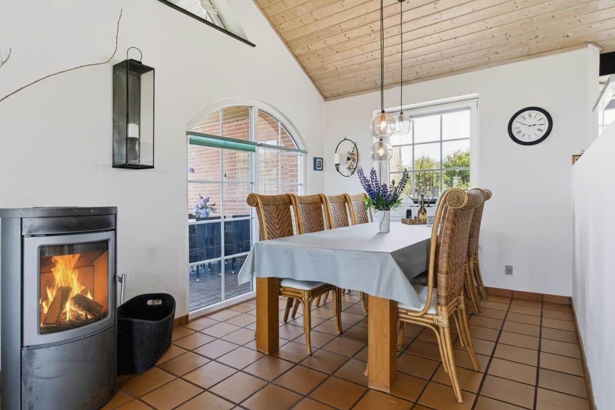 Esszimmer mit Holztisch, Rattanstühlen und Kaminofen. Terrasse über Glastür zugänglich.