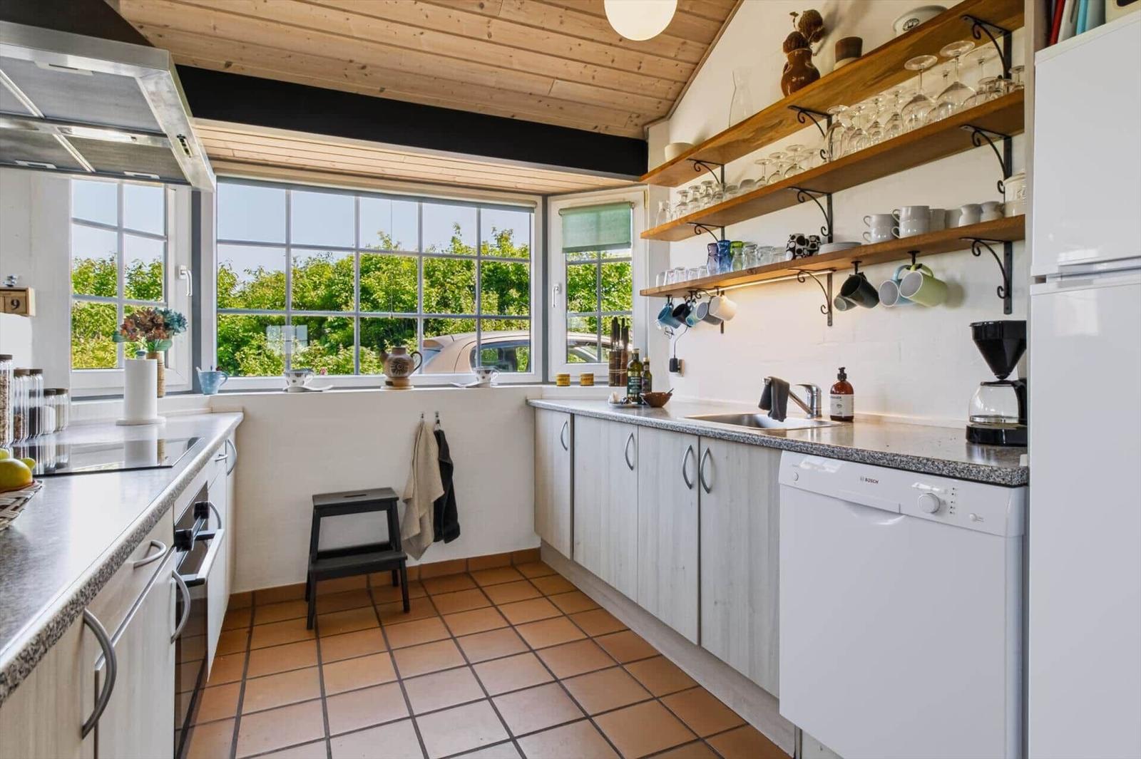 Küche mit Holzdecke, großen Fenstern und Küchenzeile mit Spüle und Geschirr.