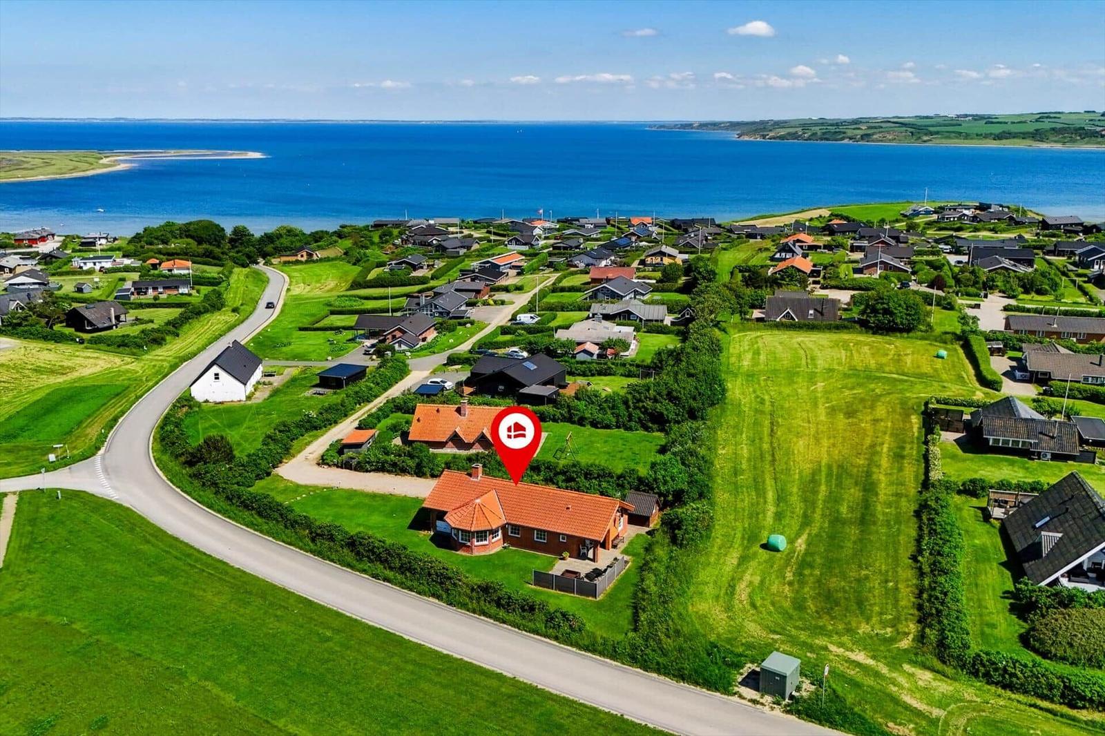 Haus mit rotem Dach liegt an einer Straße neben Grünflächen und einem See.