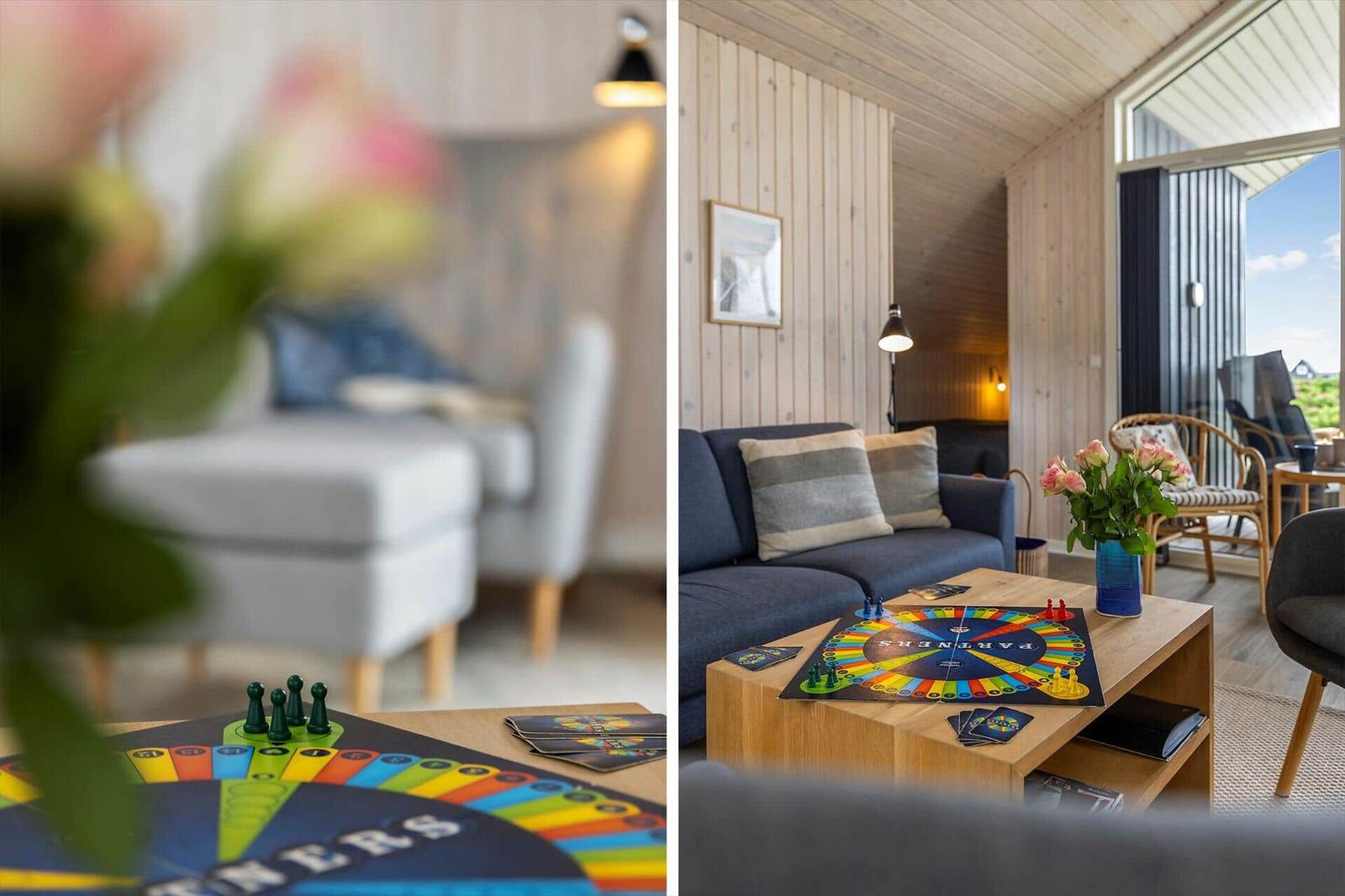 Wohnzimmer mit Sofa, Tisch und Spiel. Holzwand und Balkonansicht.
