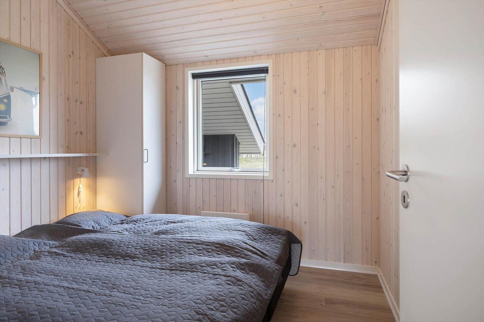 Schlafzimmer mit Holzwand, Bett und Fenster. Tür und Kleiderschrank sind sichtbar.