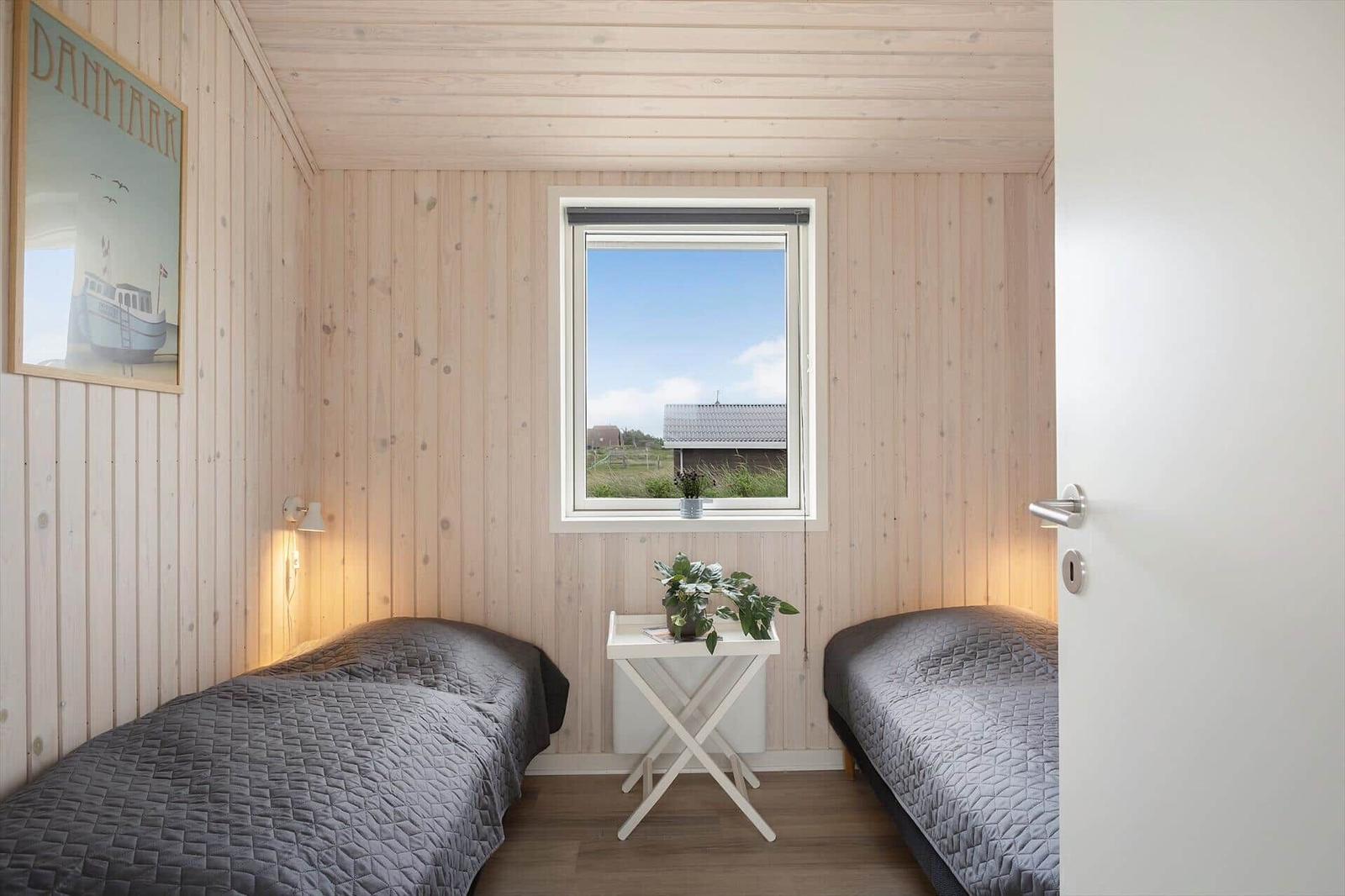 Zimmer mit zwei Betten, Holzwand und Fensterblick auf Dach und Gras.