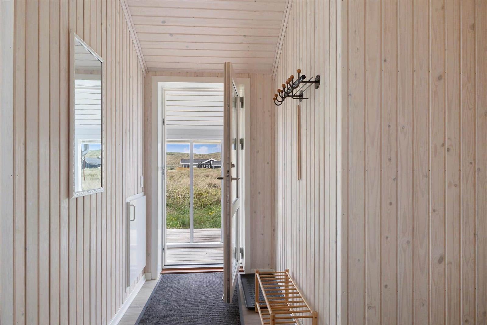 Hausflur mit Holzwand, Spiegel und Tür zum Balkon. Holzstuhl und Haken an der Wand.