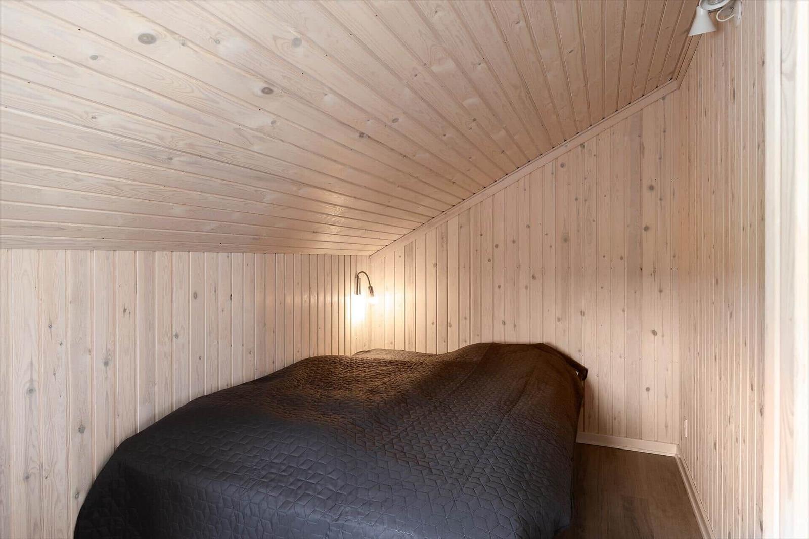 Schlafzimmer mit Holzwandverkleidung und Bett mit dunkler Bettwäsche.