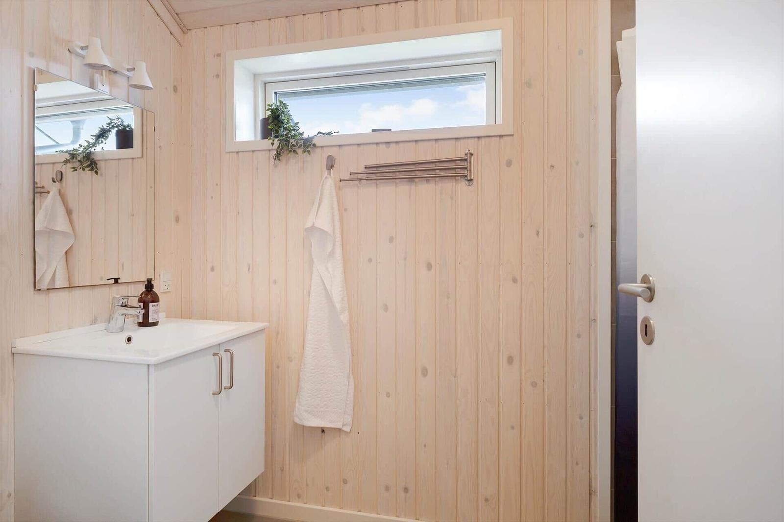 Badezimmer mit Holzwand, Waschbecken, Spiegel und Fenster