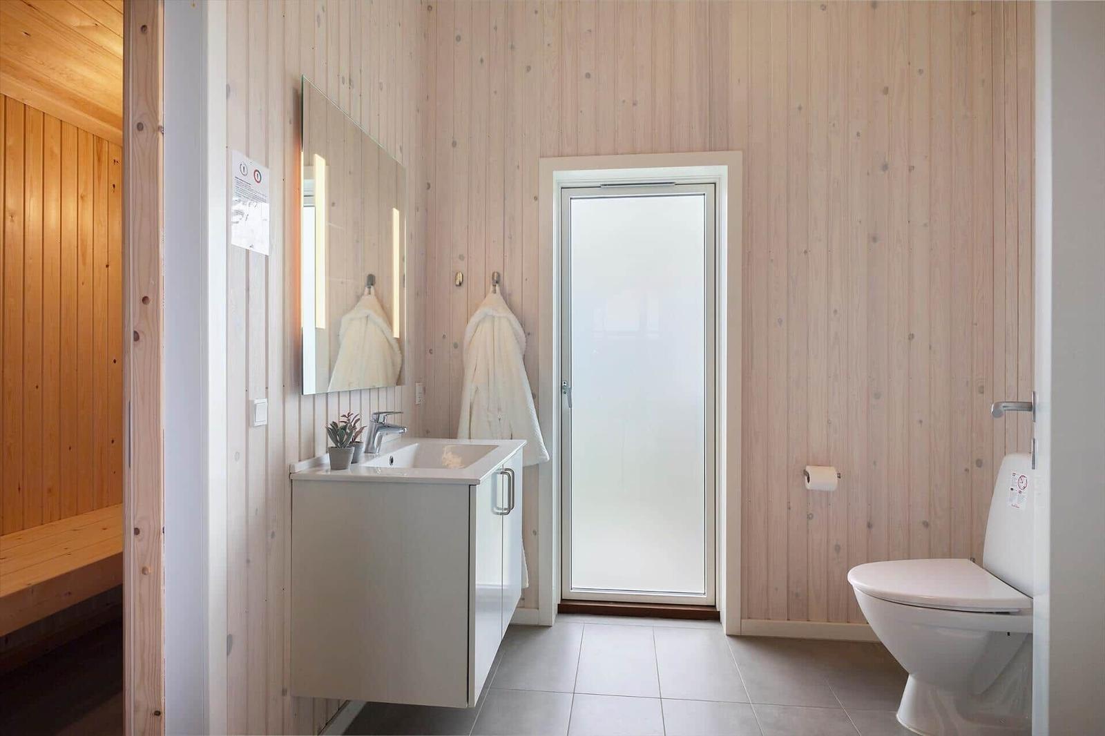 Bad mit Waschbecken, Toilette und Dusche. Holzwand und Spiegel sichtbar.