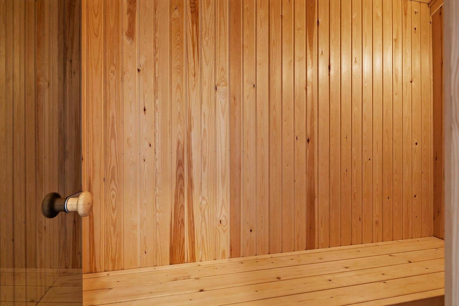 Sauna mit Holzwand und Sitzbank. Holztür mit Knauf sichtbar.