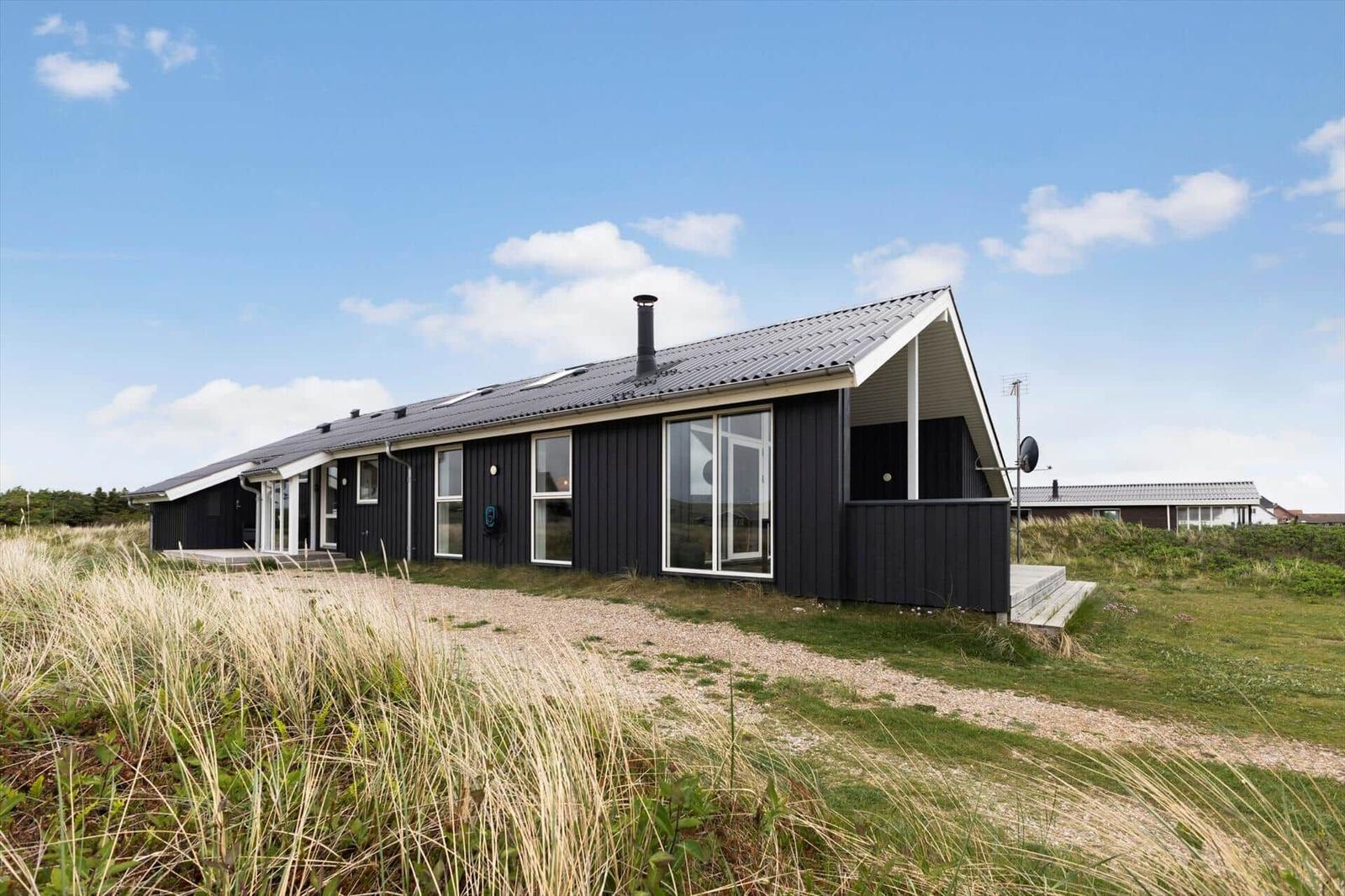 Moderne, schwarz getäfelte Villa mit großem Fenster und Dachgaube im Grasland.