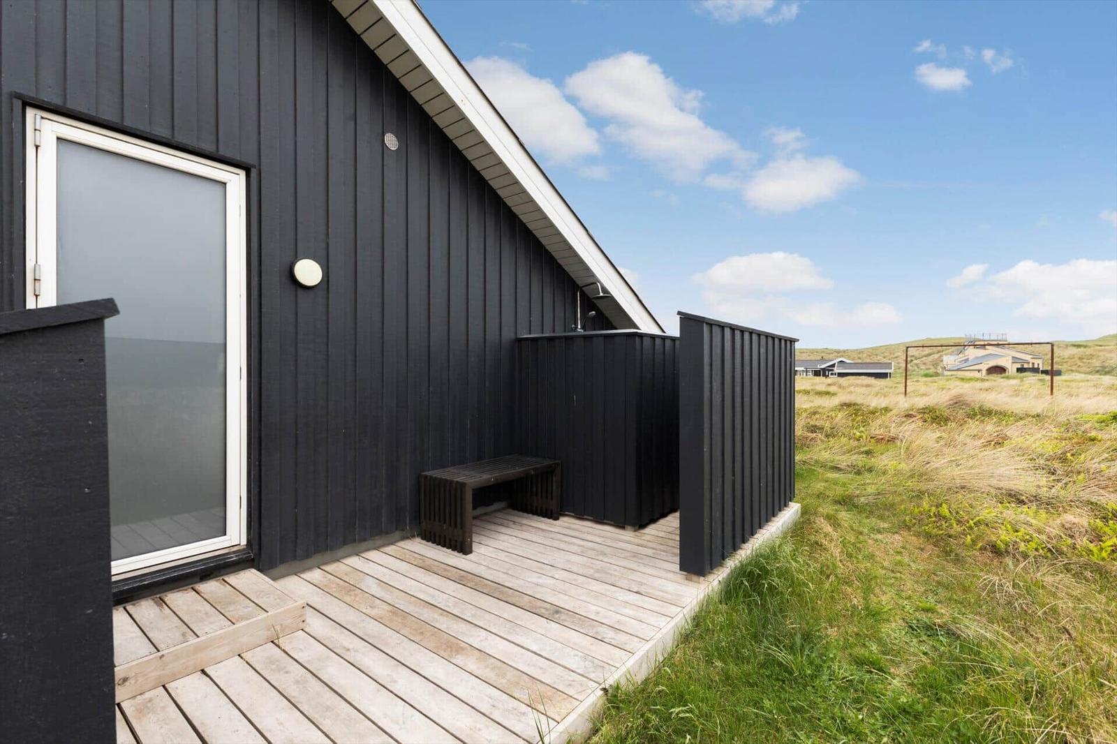 Schwarzes Holzhaus mit Terrasse und Sitzbank im Grasland.