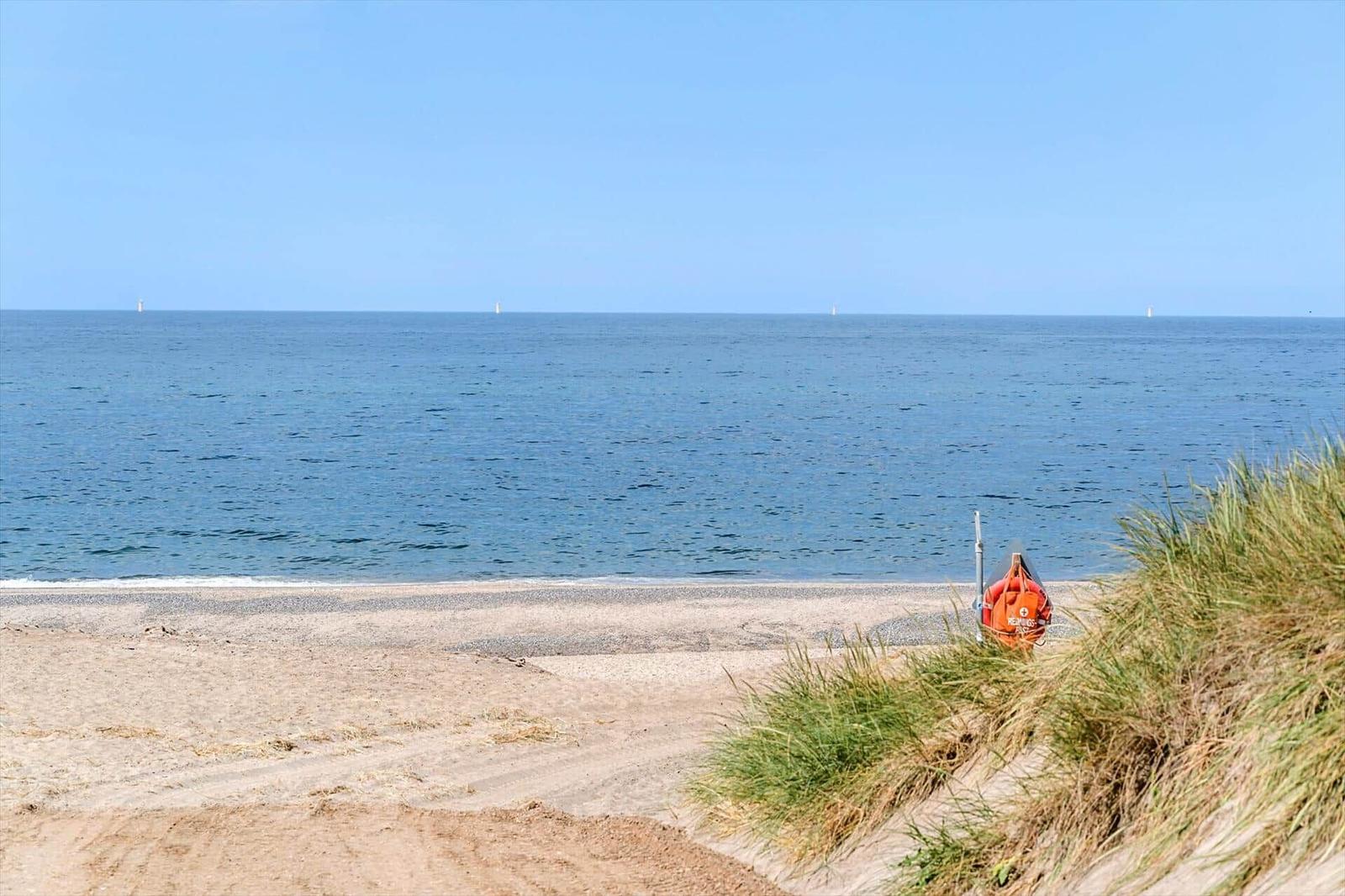 Strand mit Sand, Dünen und blauem Meer. Rettungsboot steht am Ufer.