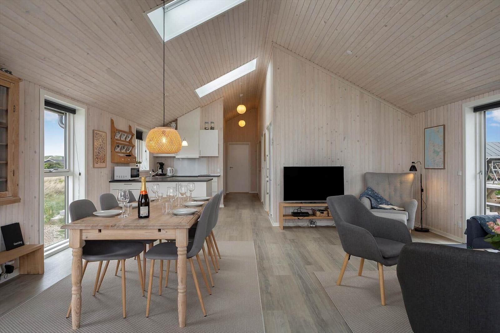 Wohn- und Essbereich mit Holzwand, Tisch, Stühlen und TV.