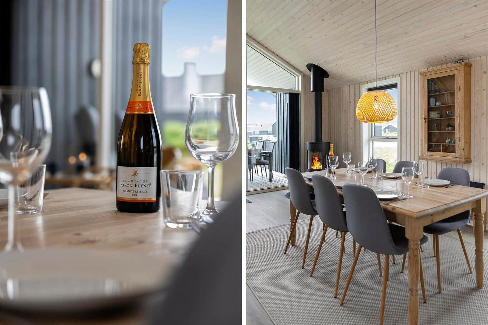Esstisch mit Stühlen, Kamin und Fensterblick. Flasche Champagner und Gläser auf Tisch.