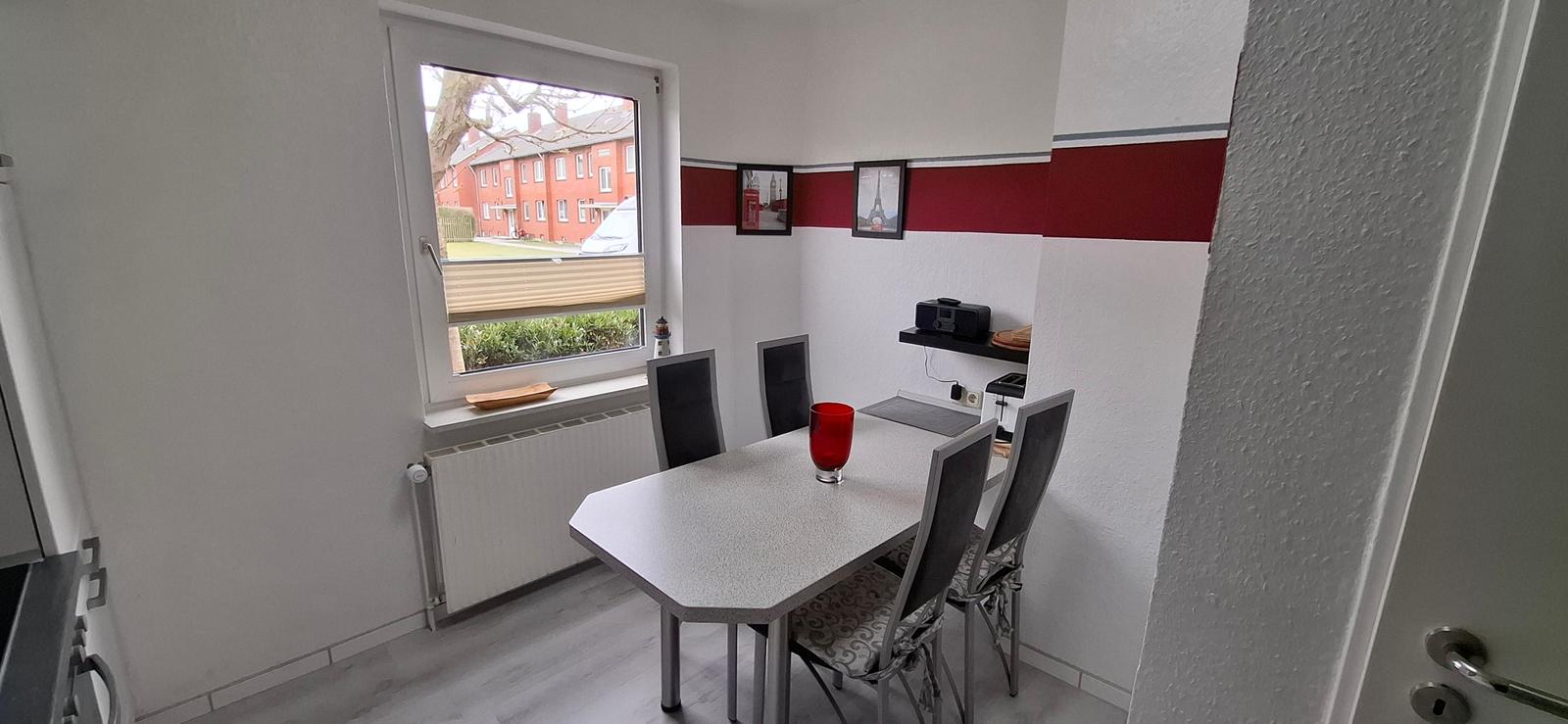Esszimmer mit Tisch, Stühlen und Fensterblick auf Wohnhaus.