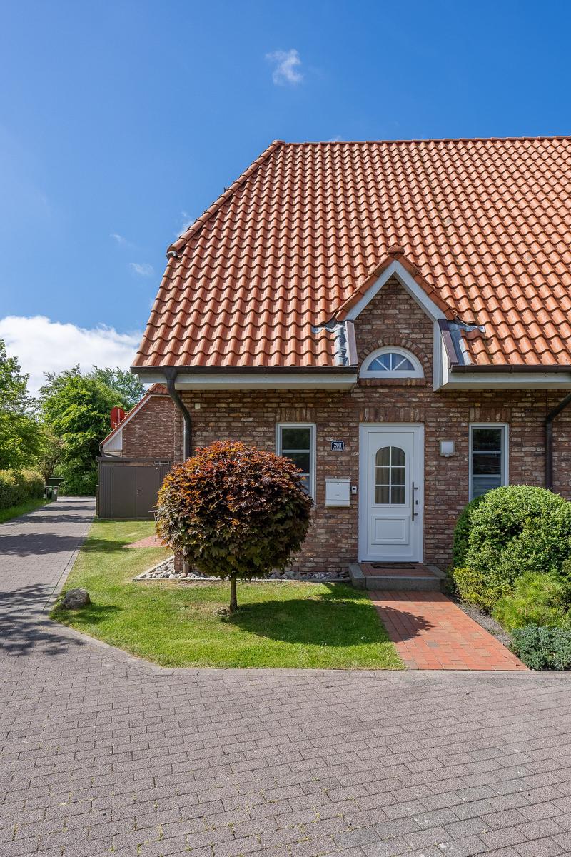 Haus mit Ziegeldach, weiße Tür und gepflegtem Vorgarten mit Rasen und Bäumen.