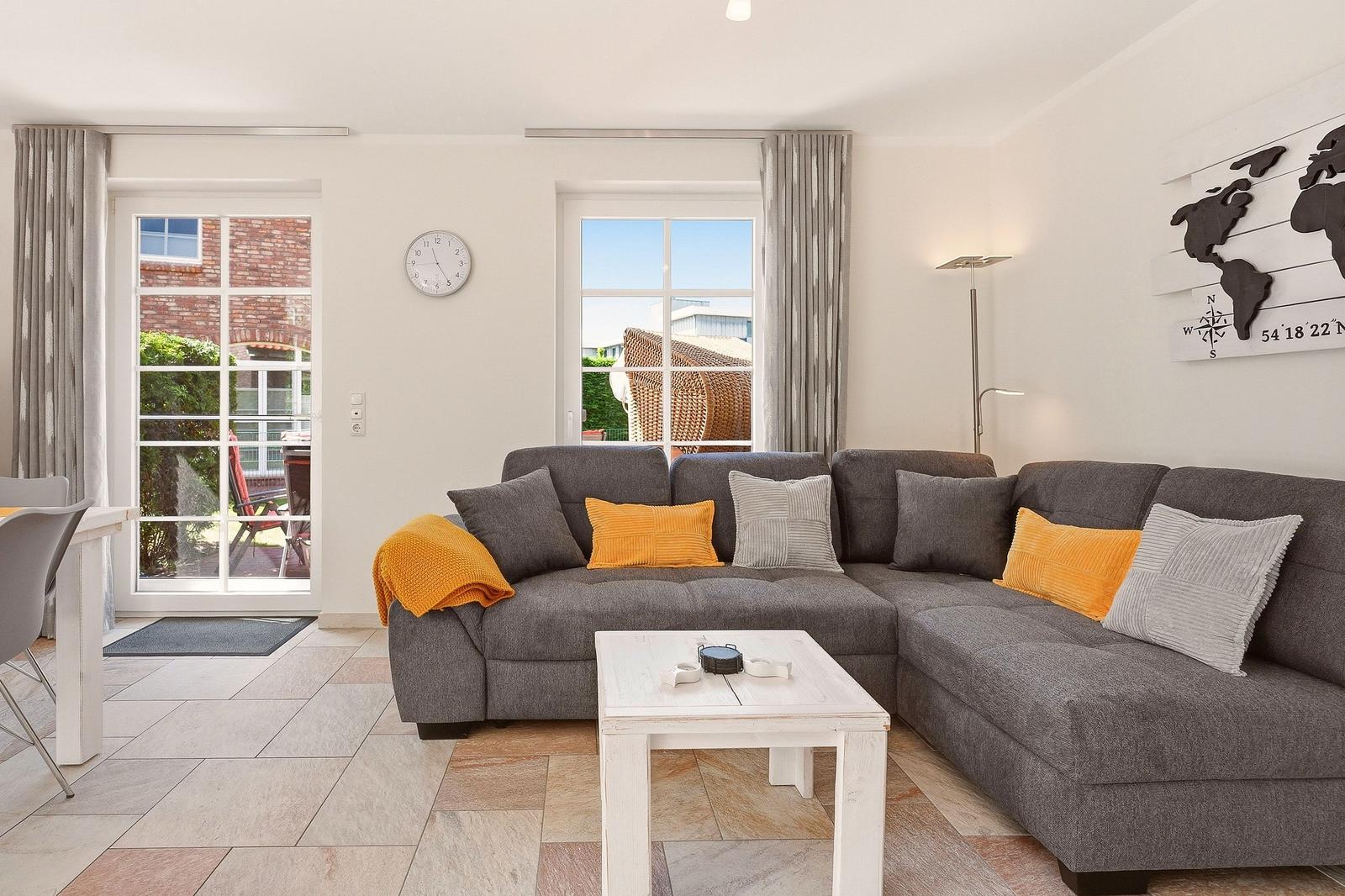 Wohnzimmer mit grauem Ecksofa, weißem Tisch und Fenstern zum Garten.