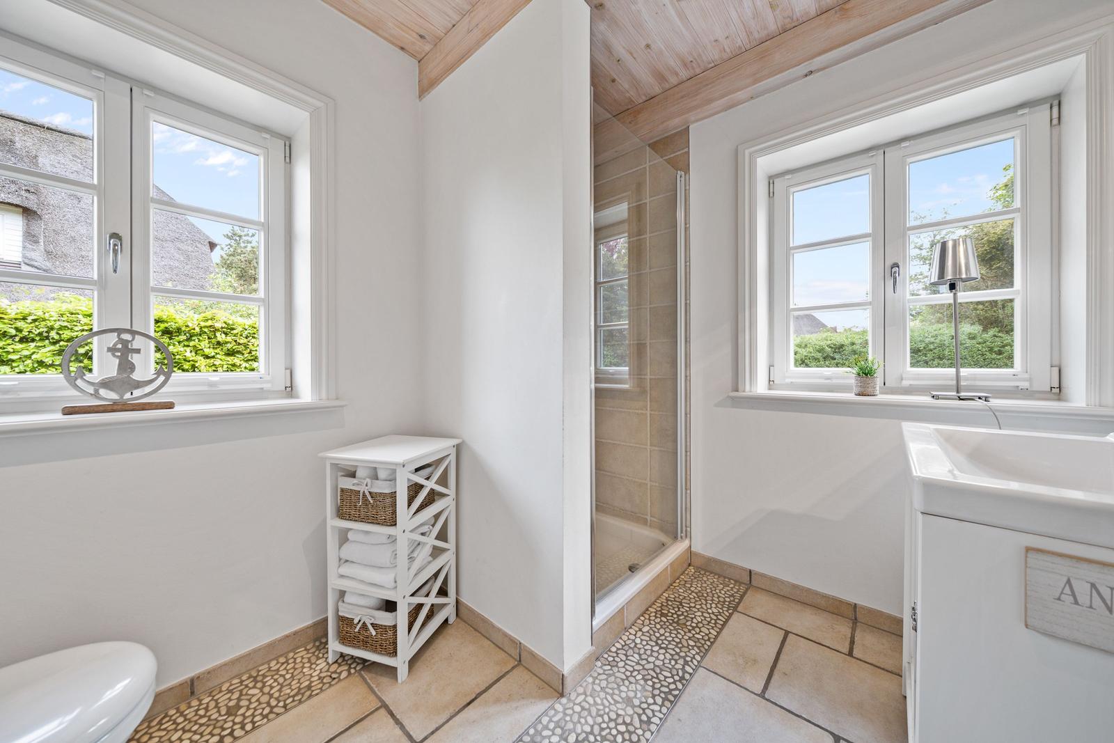 Badezimmer mit Dusche, Waschbecken und Fenstern. Holzdecke und Fliesenboden.