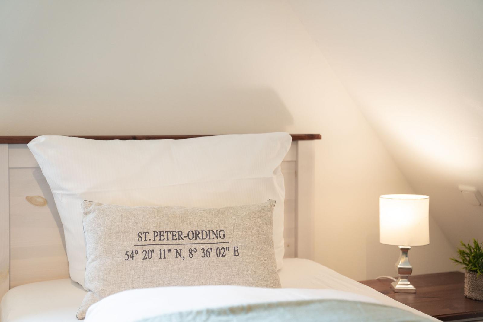 Ein Bett mit Kissen, das die Koordinaten von St. Peter-Ording zeigt.