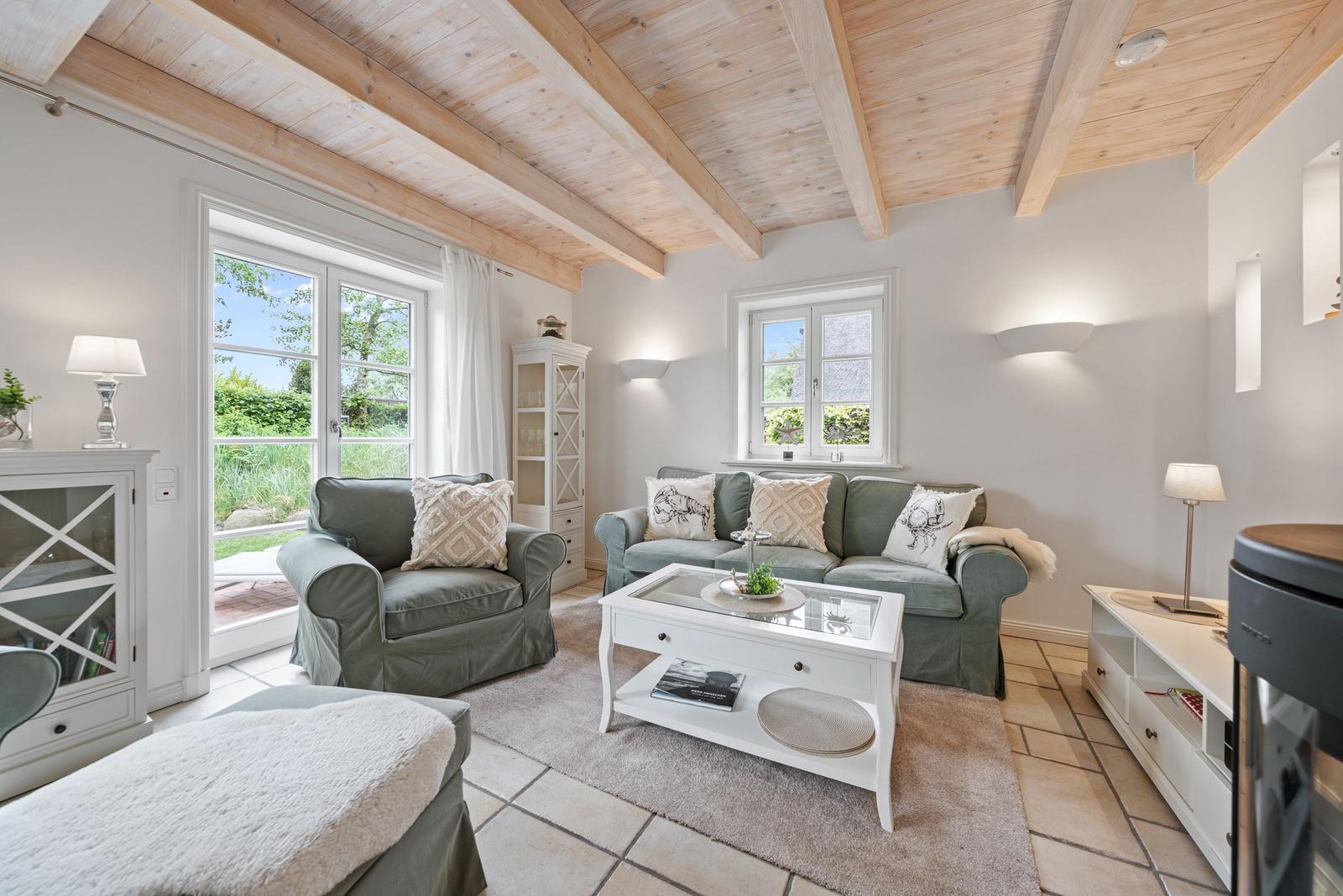 Wohnzimmer mit grünen Sitzmöbeln, weißem Couchtisch und Holzbalkendecke.