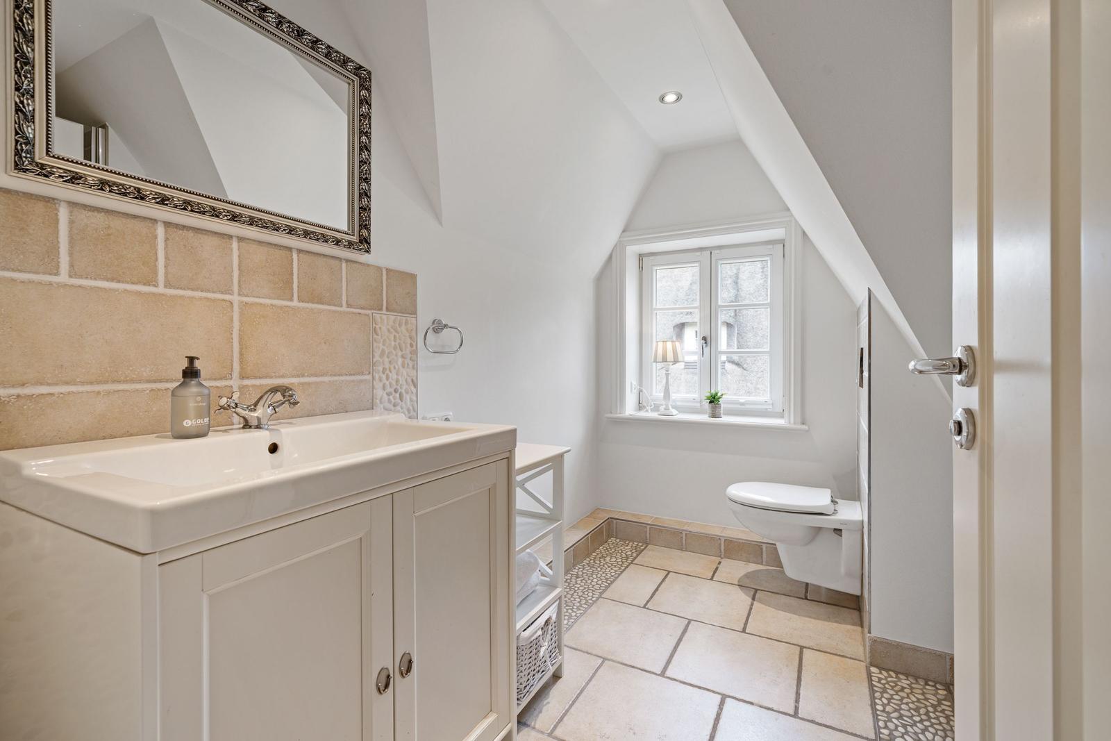 Badezimmer mit Waschbecken, Spiegel, Toilette und Fenster.