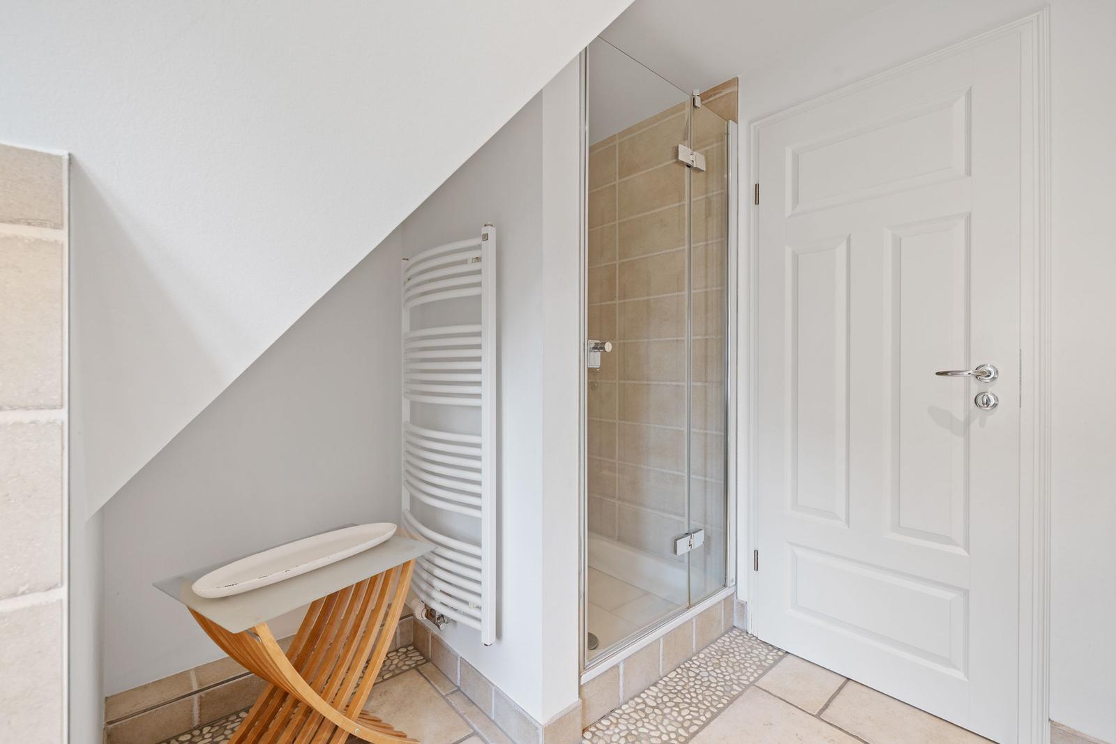 Dusche mit Glaswand, weiße Tür und Heizkörper an der Wand.
