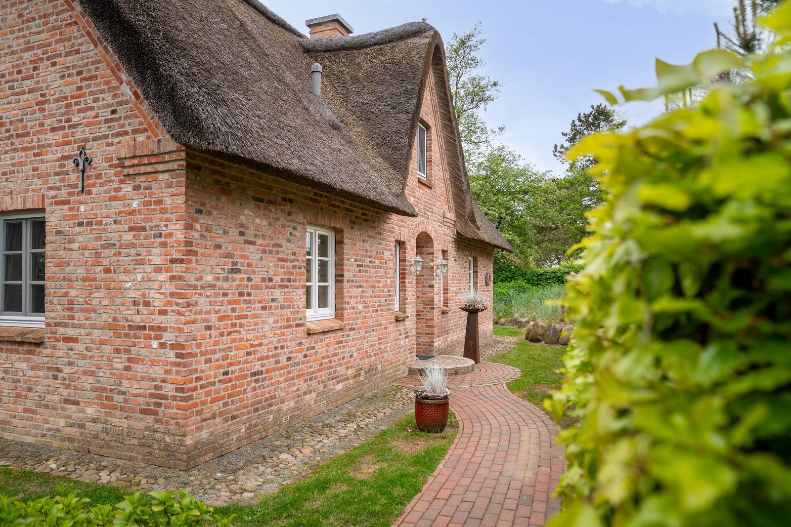 Rotes Backsteinhaus mit Strohdach und gepflastertem Weg durch grünen Garten.
