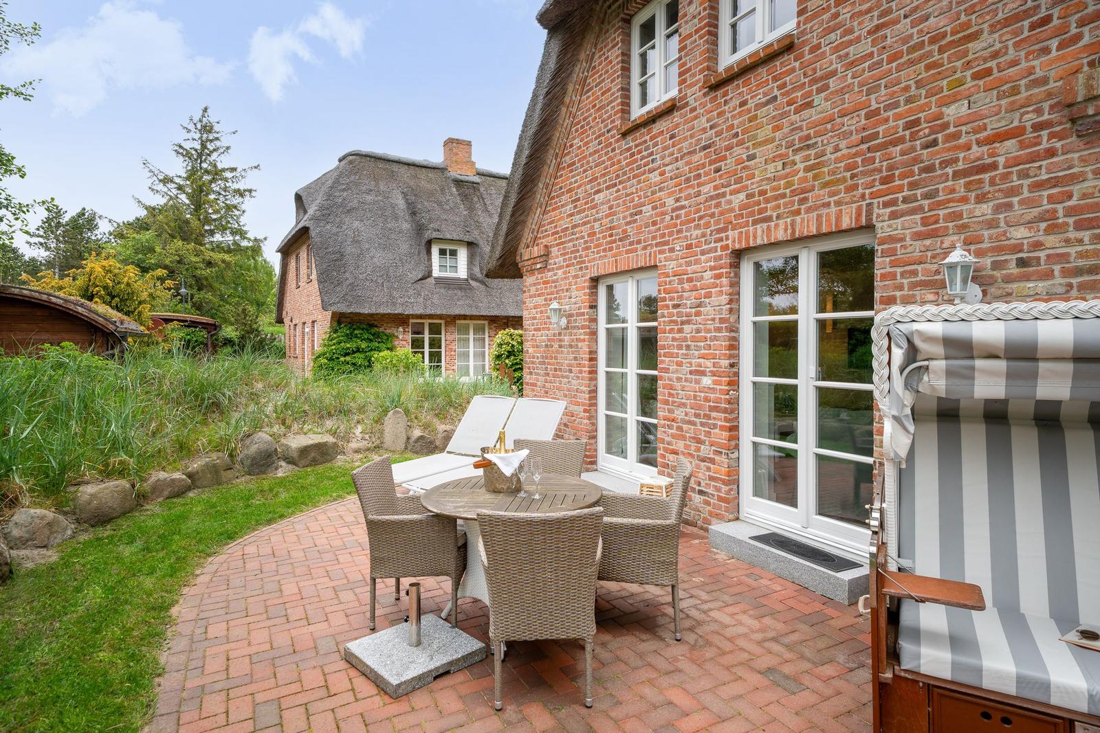 Terrasse mit Sitzgruppe und Liegestühlen vor Backsteinhaus mit Schiebetüren.