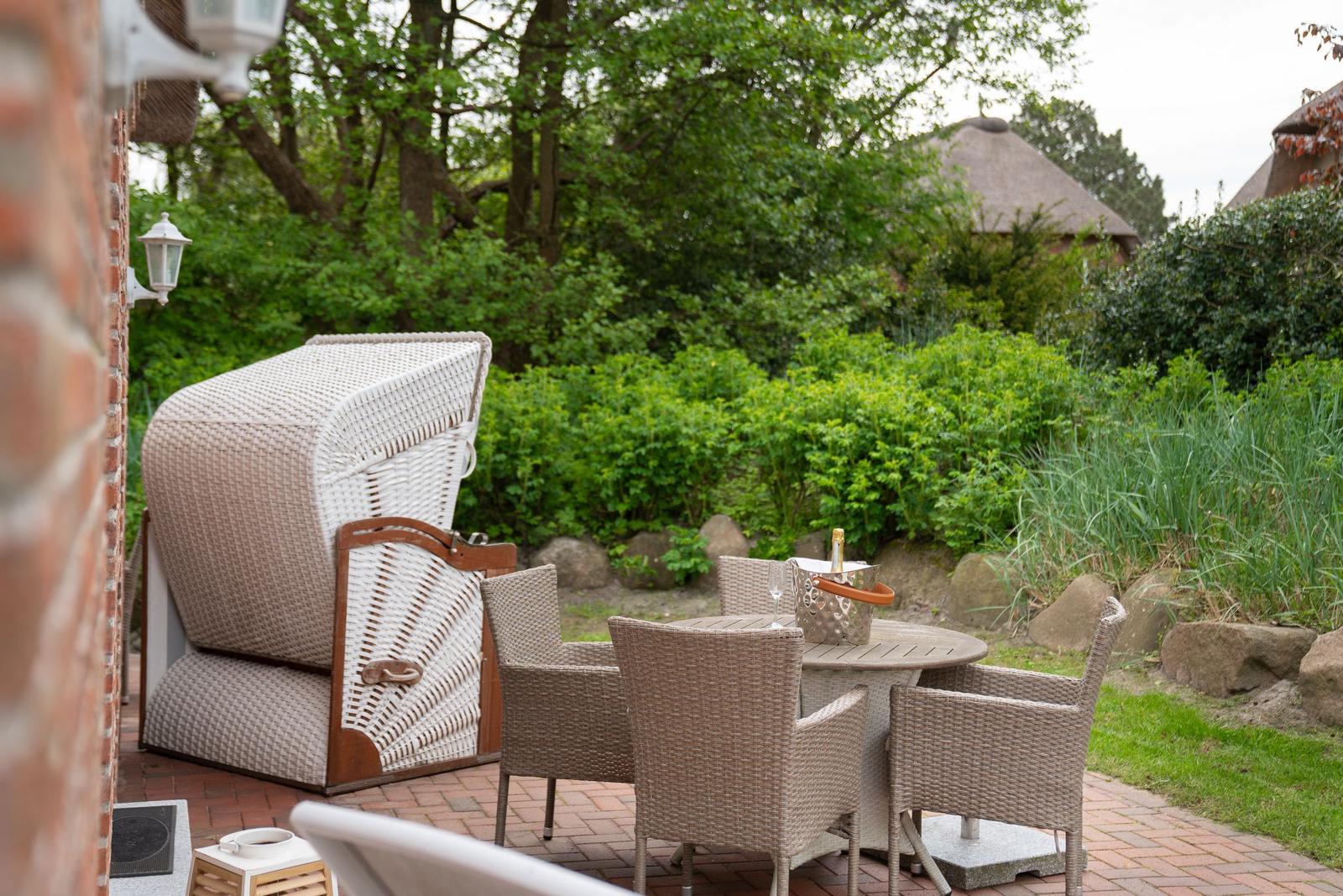 Terrasse mit Loungemöbeln, Tisch und Flasche Champagner im Garten.