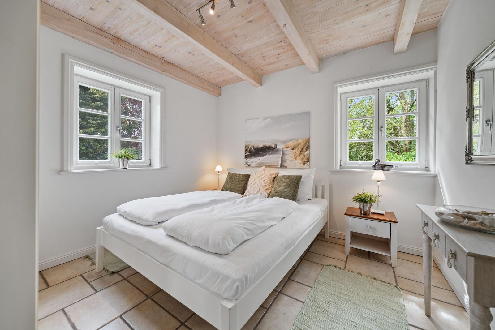 Schlafzimmer mit Doppelbett, Holzdecke, zwei Fenstern und Nachttisch.