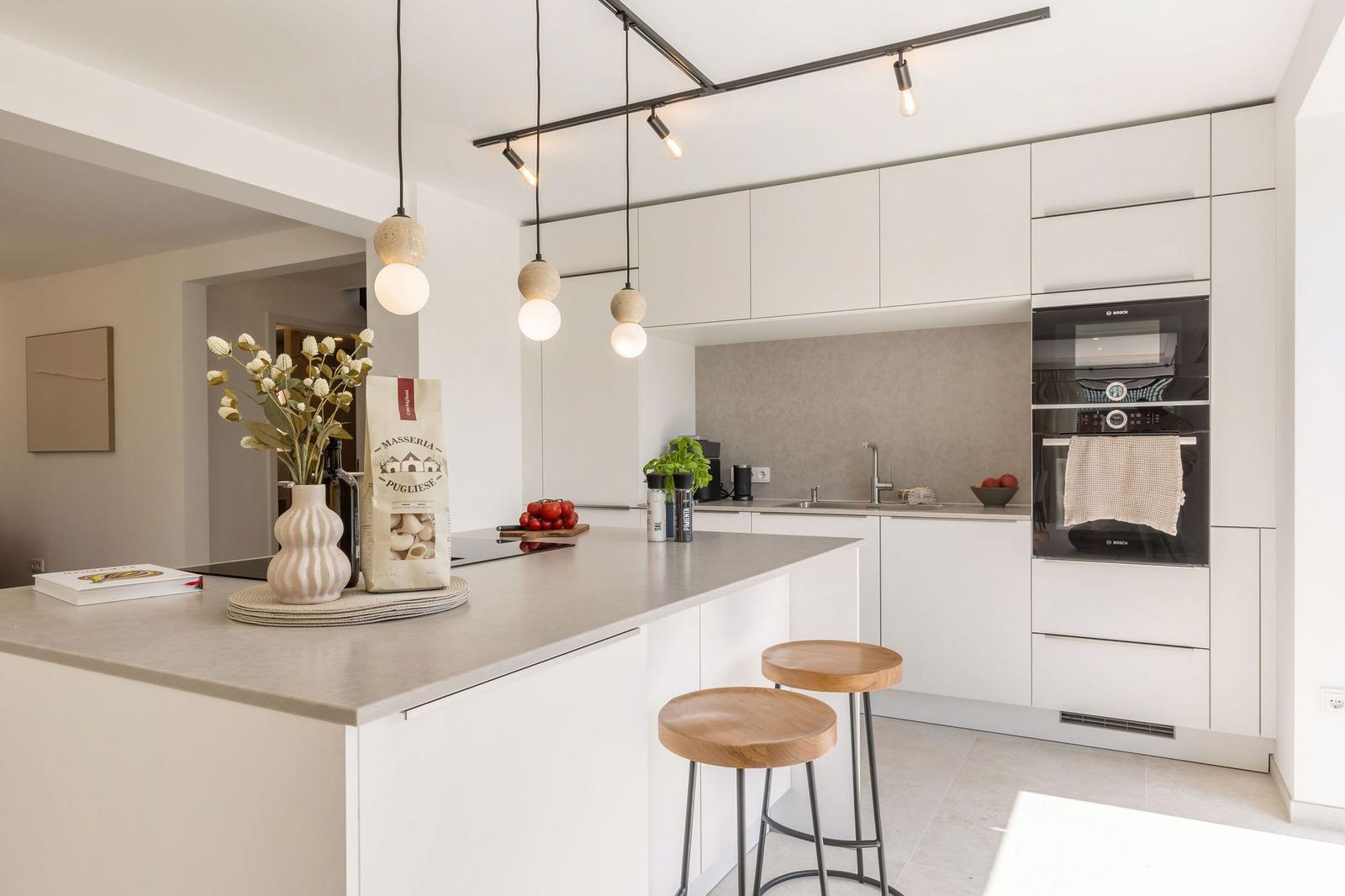 Moderne Küche mit Kücheninsel, weißen Schränken und integriertem Backofen.