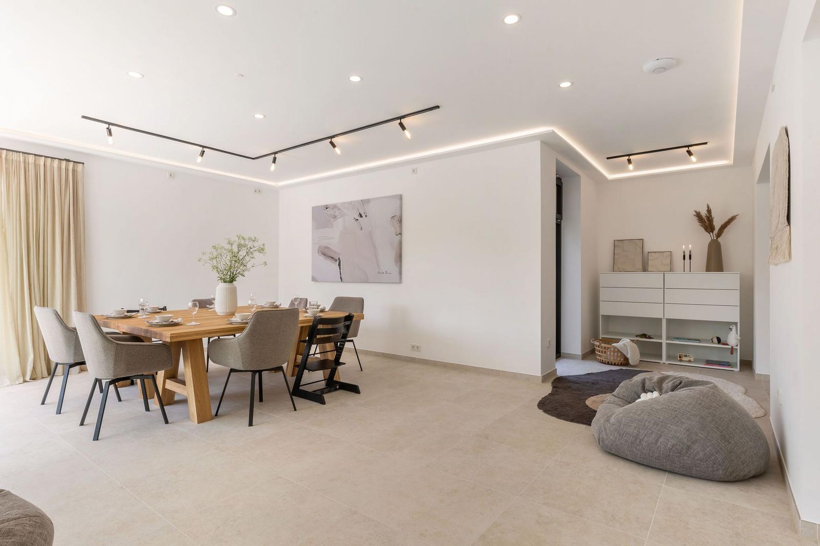 Essbereich mit Holztisch, Stühlen und Wandbild. Im Hintergrund steht ein weißer Schrank.