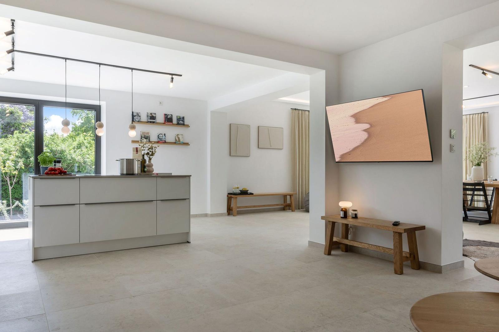 Moderne Küche mit Kücheninsel und TV an der Wand. Durchgang zu Wohn- und Essbereich.