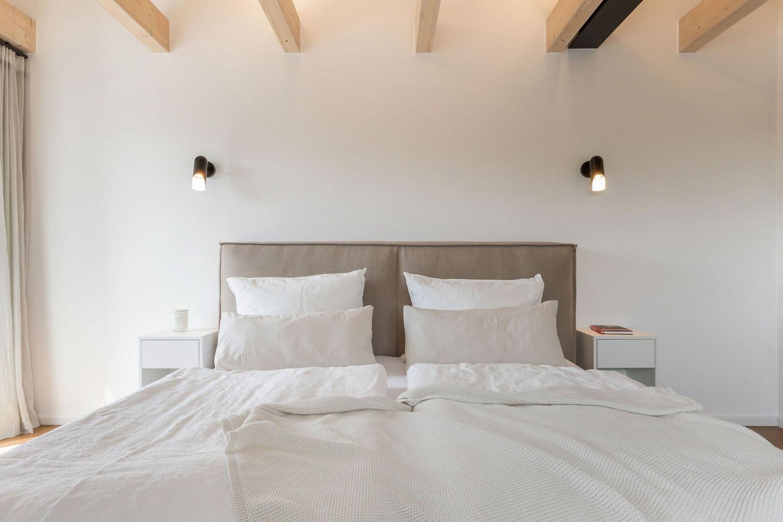 Schlafzimmer mit Bett, Nachttischen und Wandlampen unter Holzbalken.