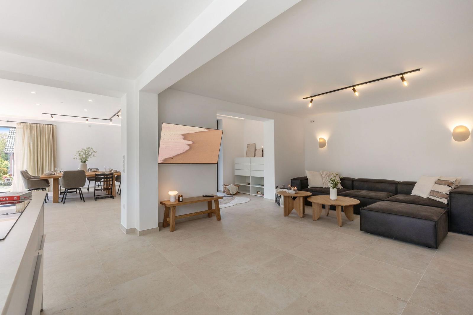 Wohnzimmer mit dunklem Sofa, Holztischen und Fernseher. Essbereich im Hintergrund.