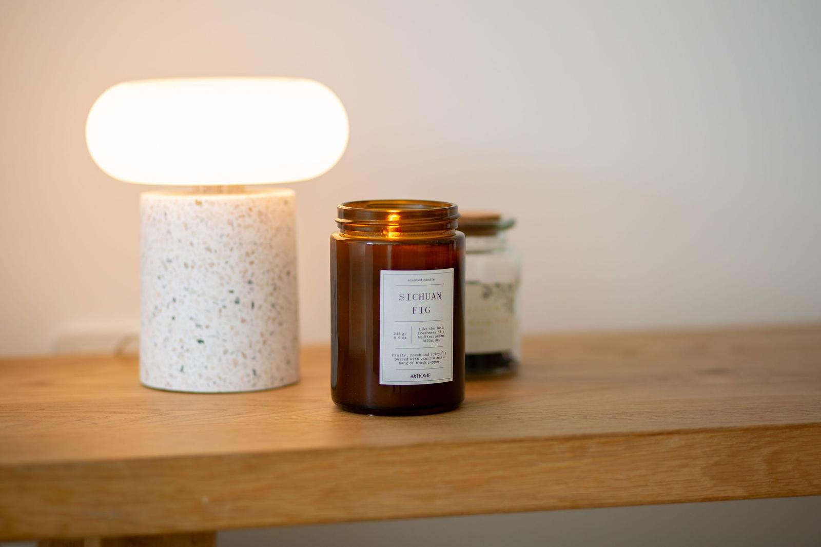Auf einem Holztisch steht eine Lampe und eine Duftkerze in einem Glas.