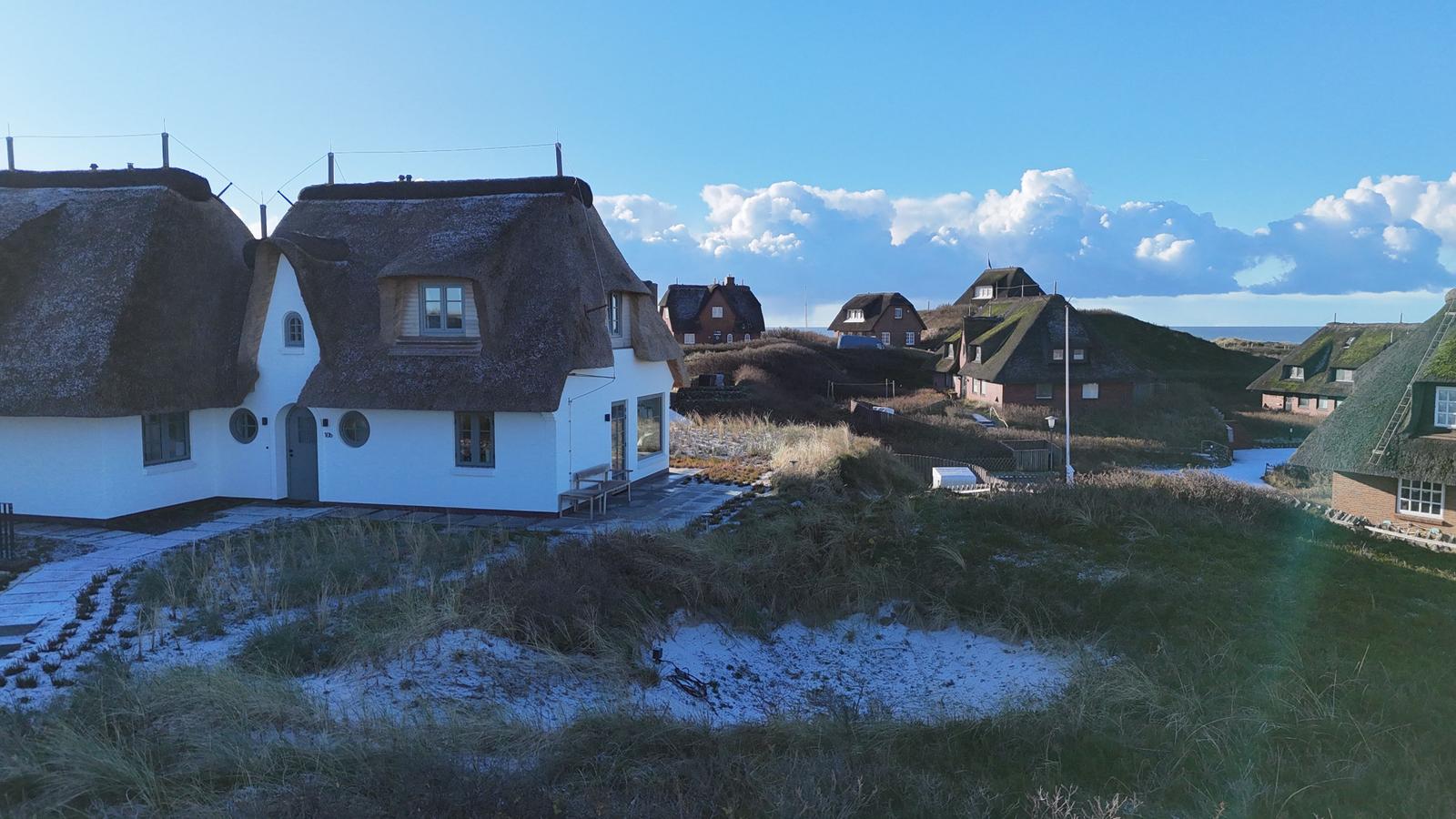 Dorf mit strohgedeckten Häusern auf Hügeln unter blauem Himmel mit weißen Wolken.