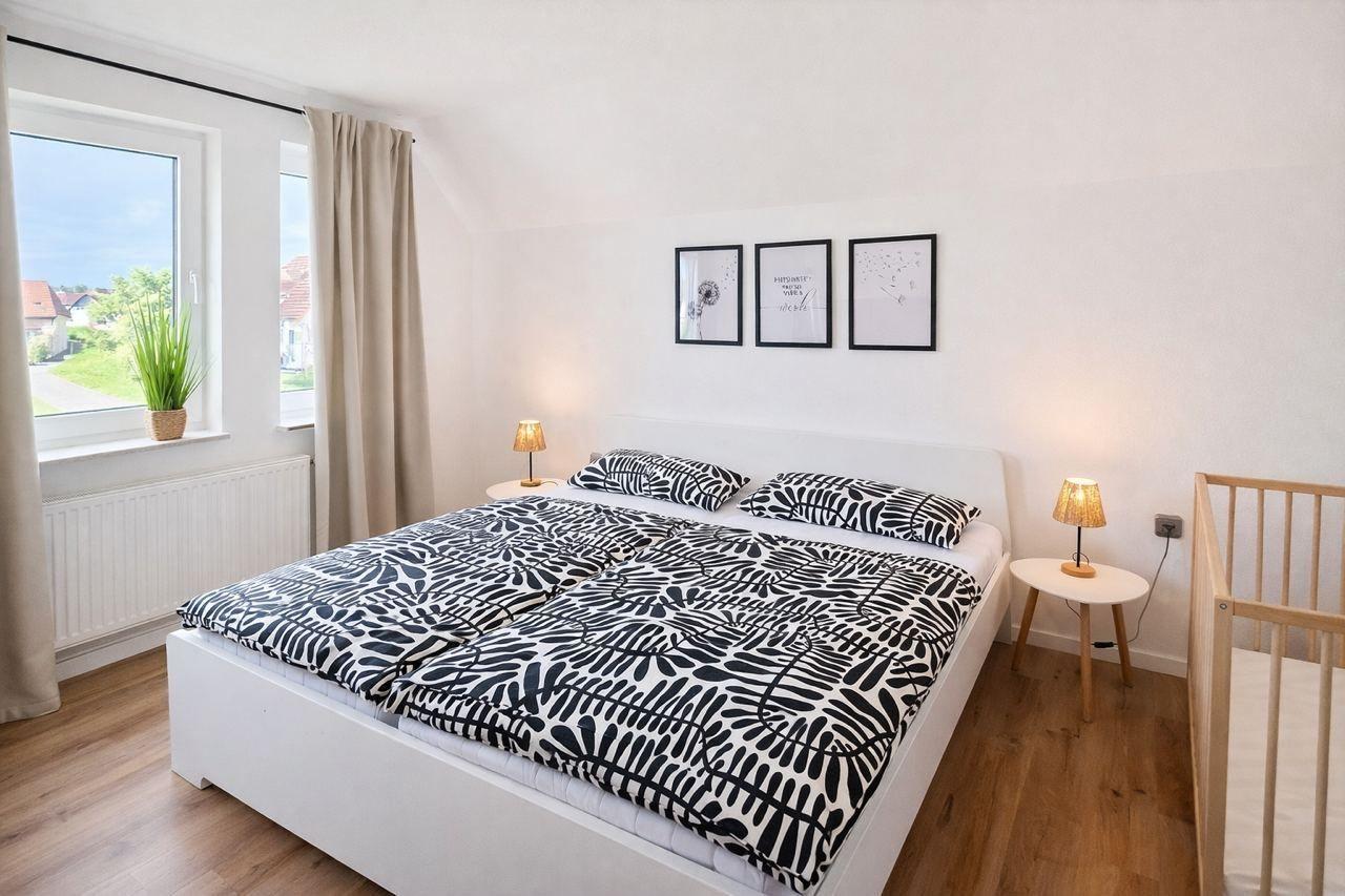 Schlafzimmer mit Doppelbett, Fenster, Nachttischen und Kinderbett.
