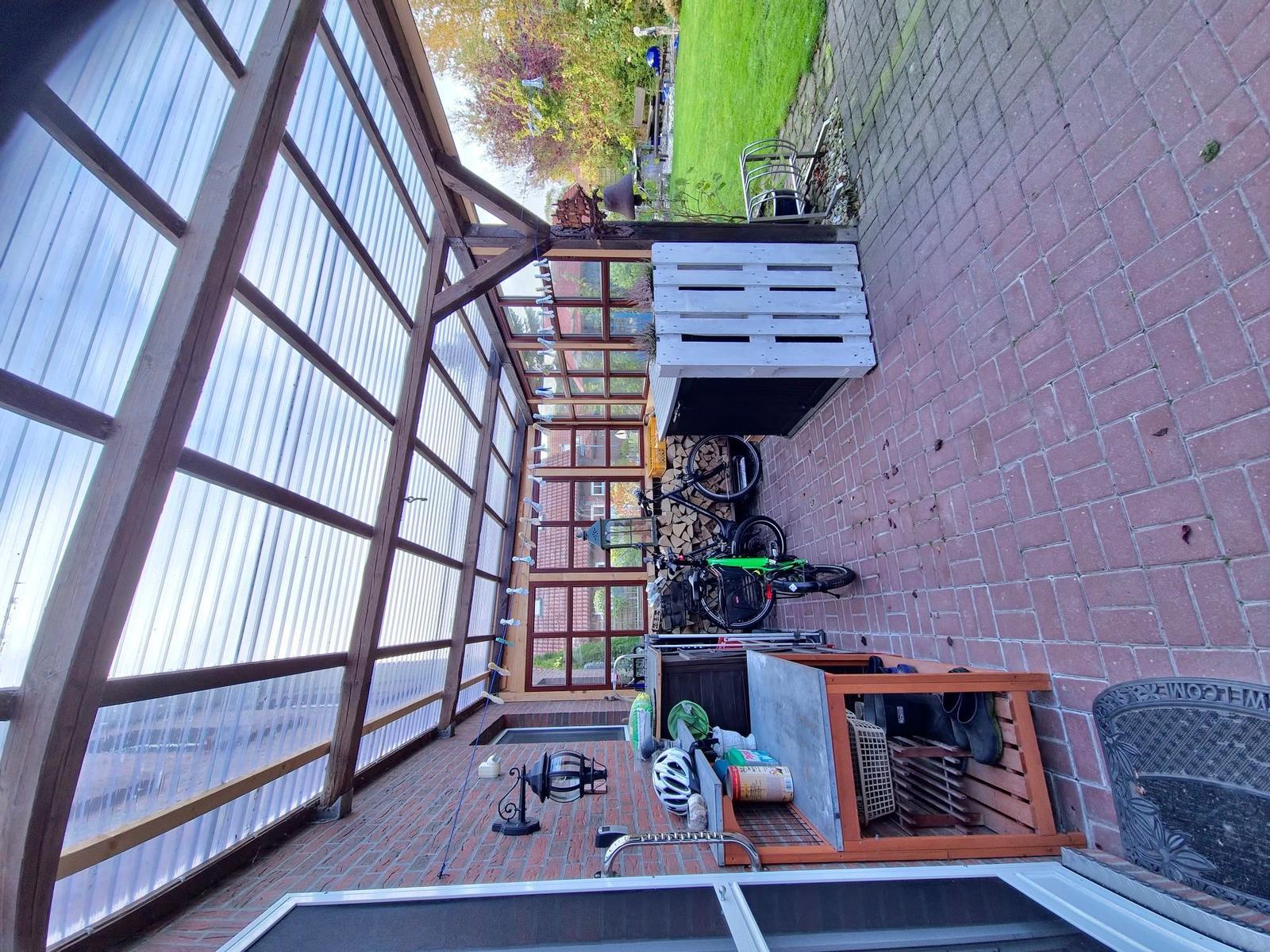 Außenbereich mit Holzkonstruktion, Fahrrad und Gartenmöbeln auf Steinplatten.