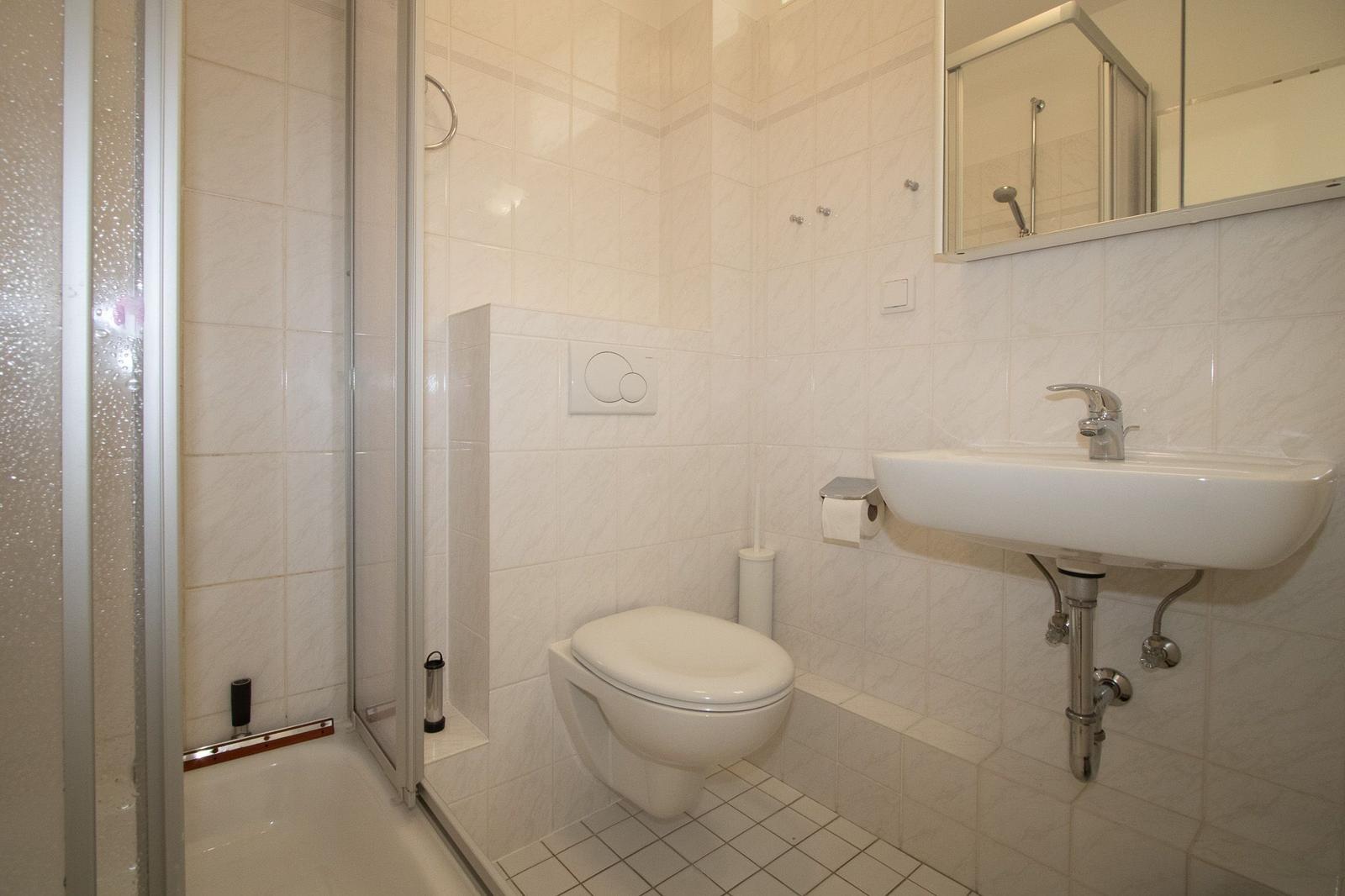 Badezimmer mit Dusche, Toilette und Waschbecken. Fliesenwand und Spiegel.