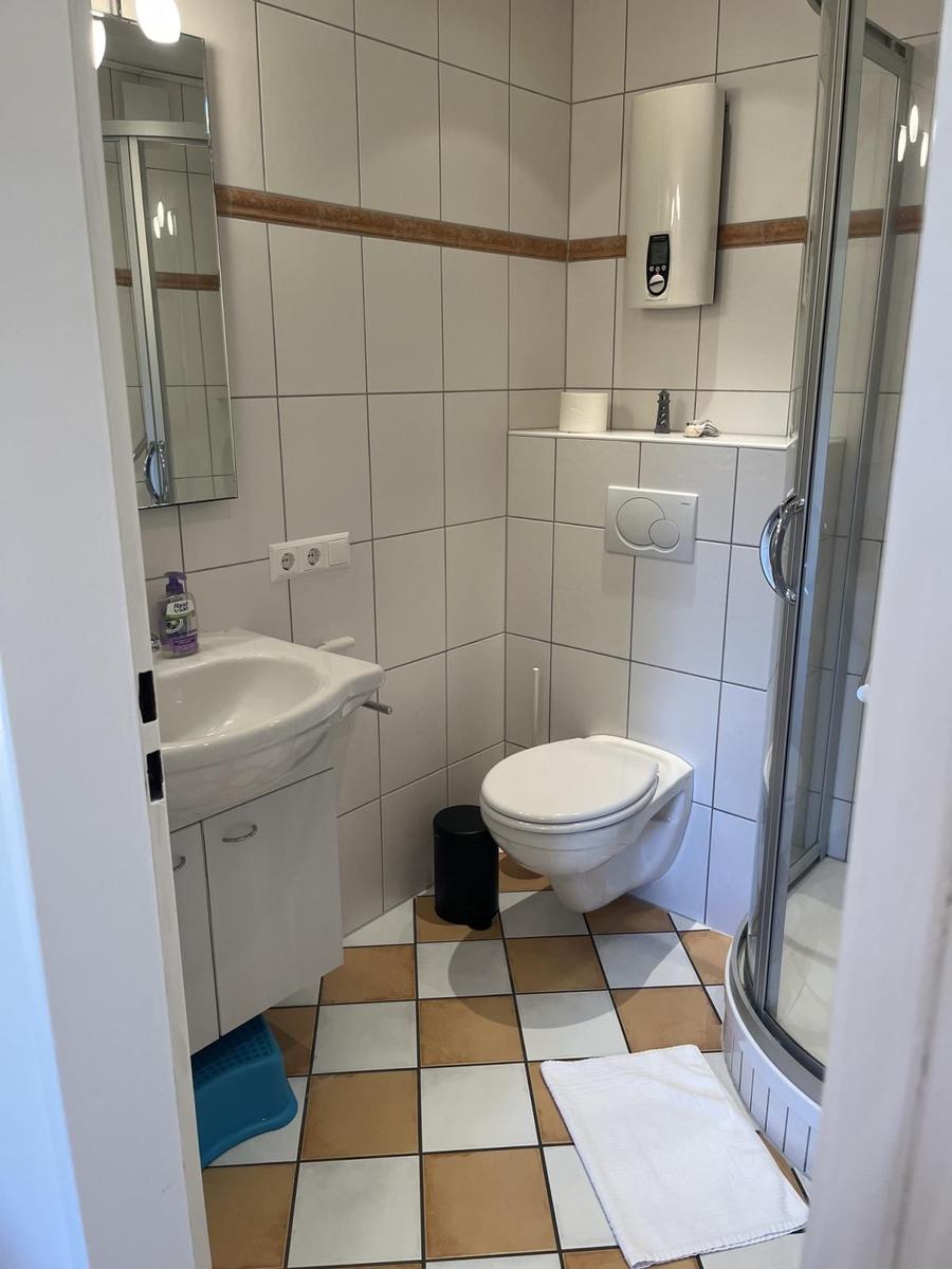 Badezimmer mit Dusche, WC und Waschbecken. Fliesenboden und Spiegel.