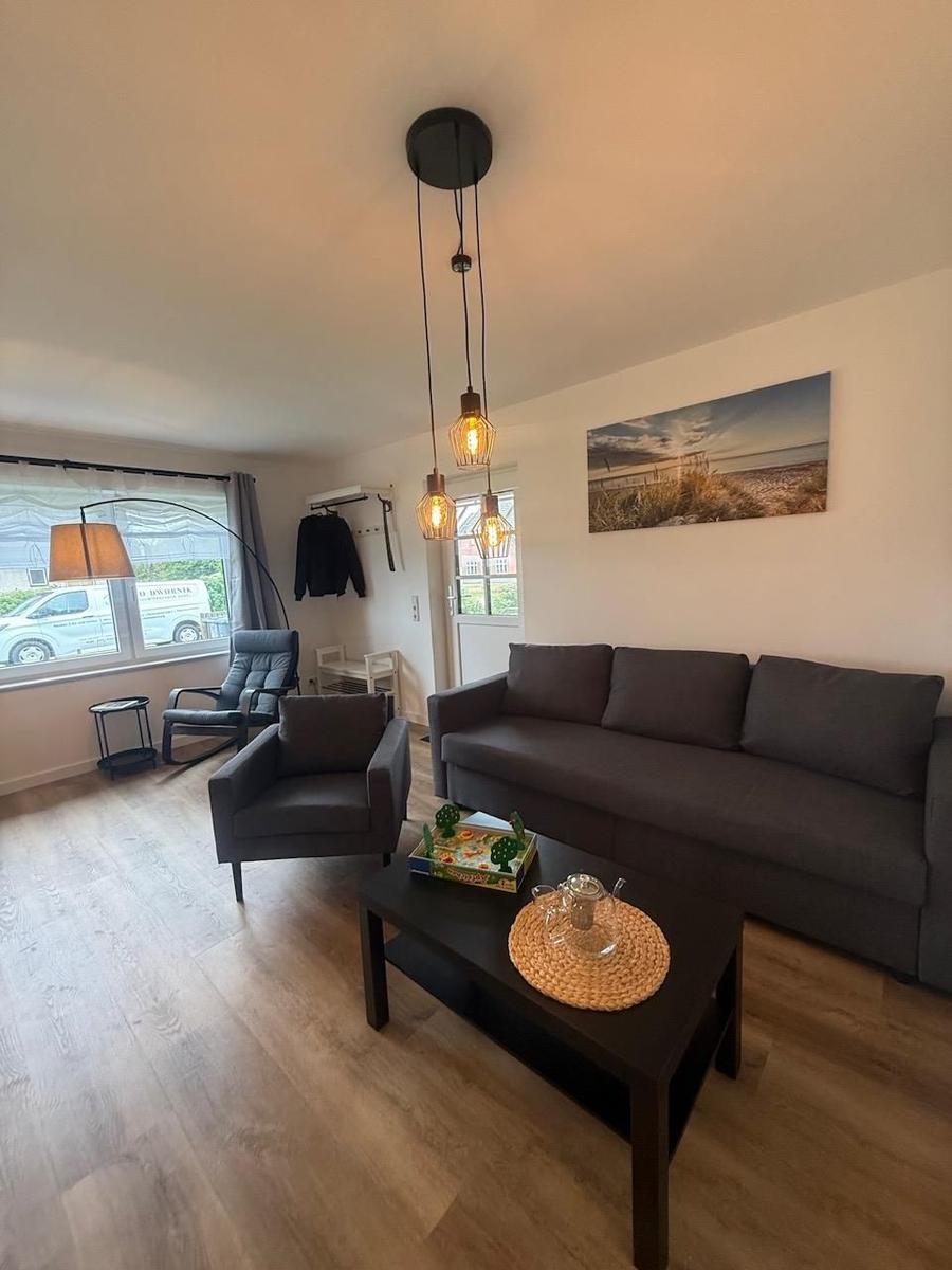 Wohnzimmer mit Sofa, Sessel und Couchtisch. Hängelampe und Wandbild sichtbar.