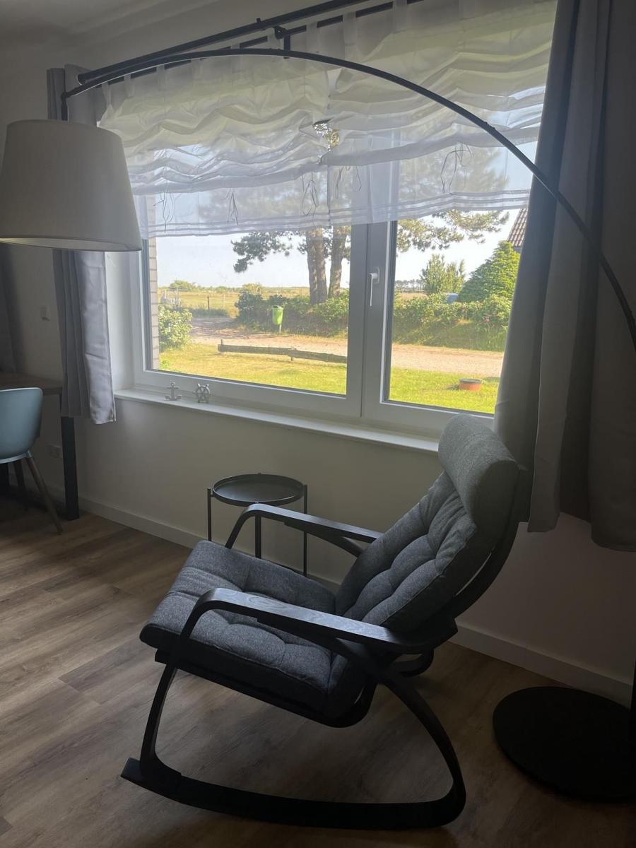 Schwankstuhl vor großem Fenster mit Blick auf Garten und Bäume.
