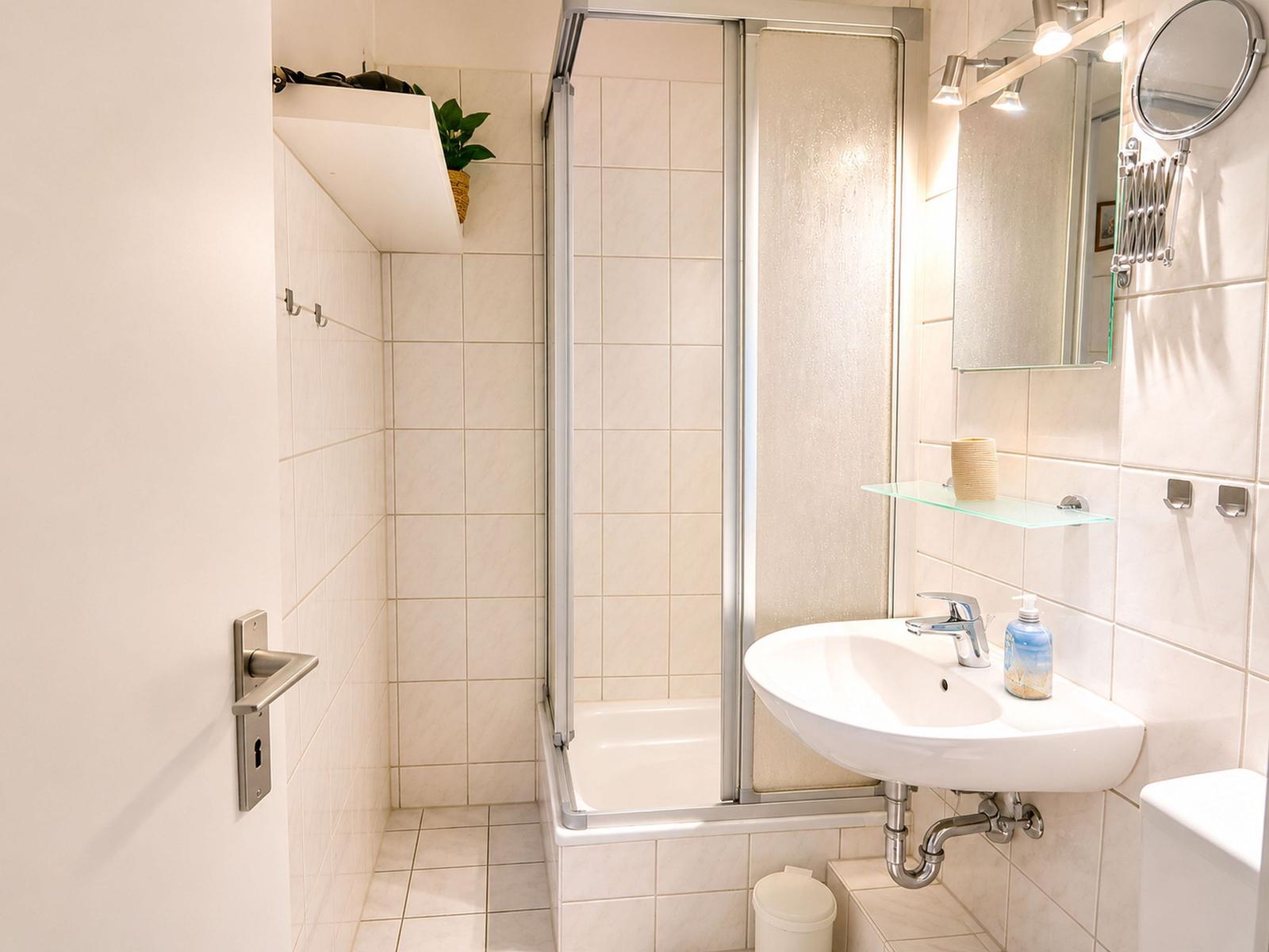 Badezimmer mit Dusche, Waschbecken und Spiegel.