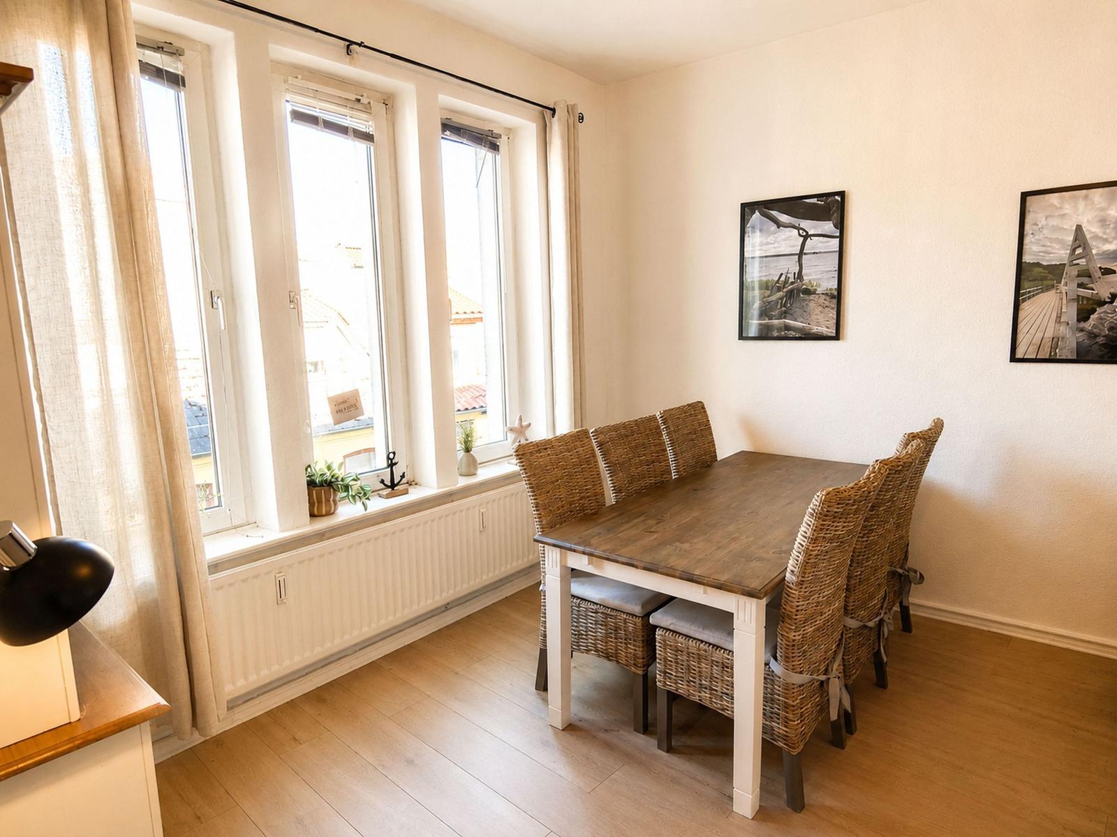 Esszimmer mit Tisch, Stühlen und Fensterfront. Wandbilder und Holzboden.